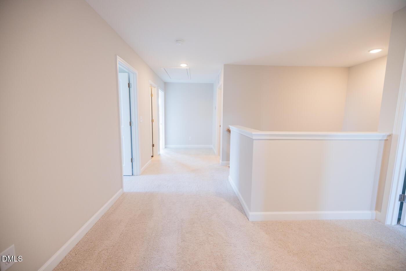 Bright upstairs hallway with beige carpet, neutral walls, open doors, and railing overlook in The Hickory II C, Zebulon, NC