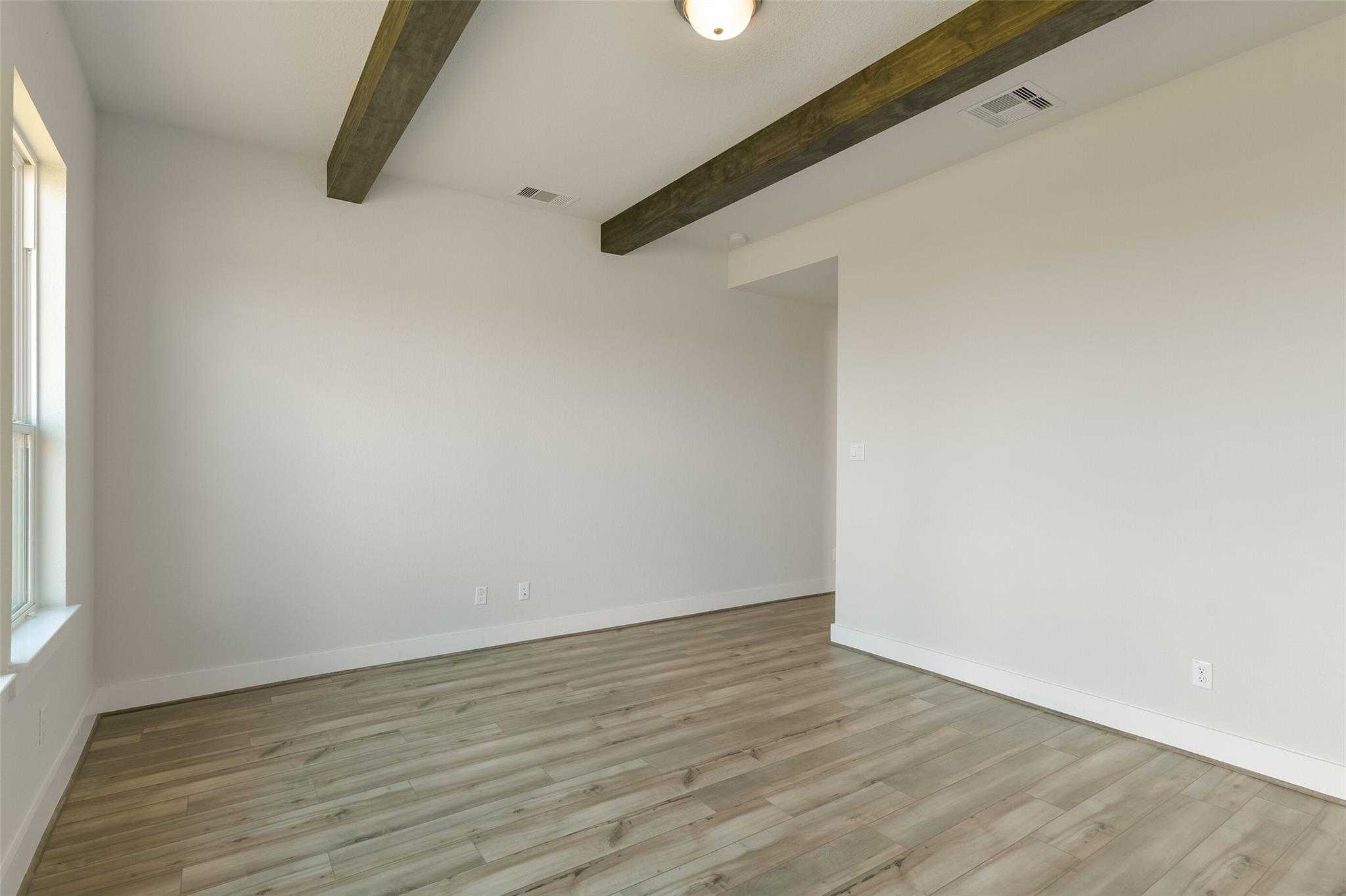 Spacious empty living area with wooden ceiling beams, large window, and light wood flooring in Davidson Homes The Edward A, Lago Mar, Texas City