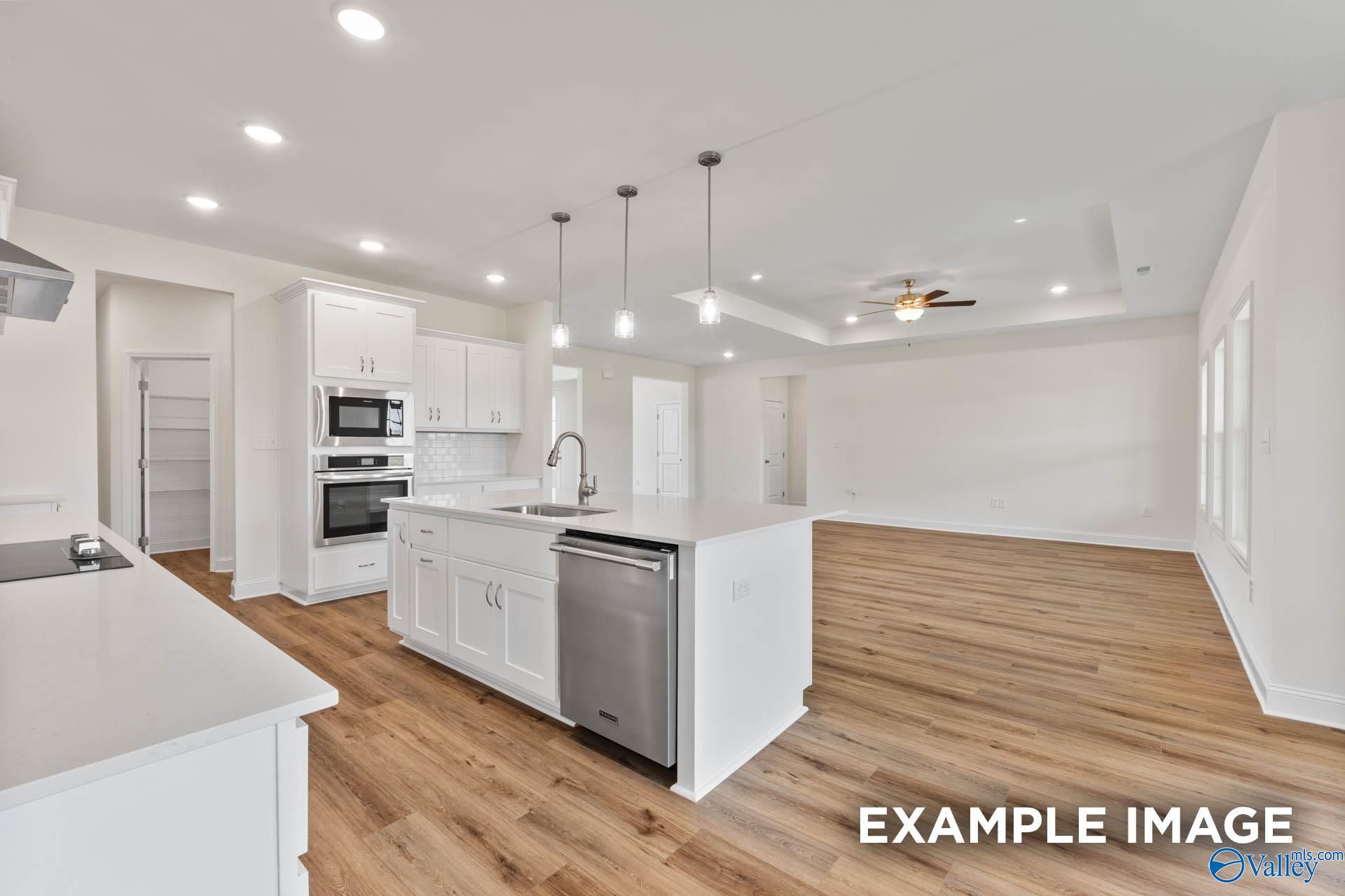Open-concept kitchen with white cabinets, quartz island, stainless dishwasher and double ovens in Davidson Homes The Emory, Toney, AL