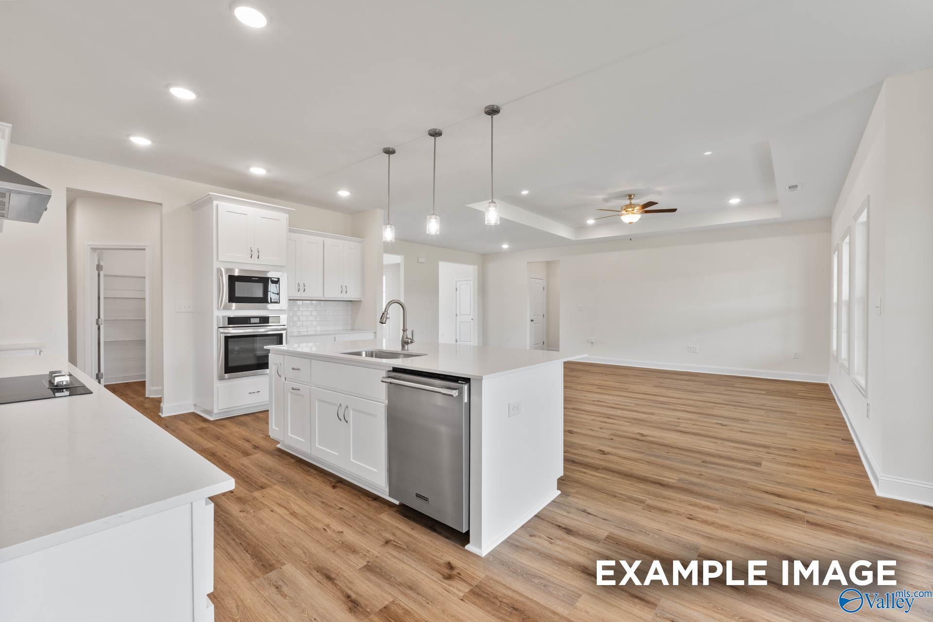 Open-concept kitchen with white cabinets, quartz island, stainless dishwasher and double ovens in Davidson Homes The Emory, Toney, AL