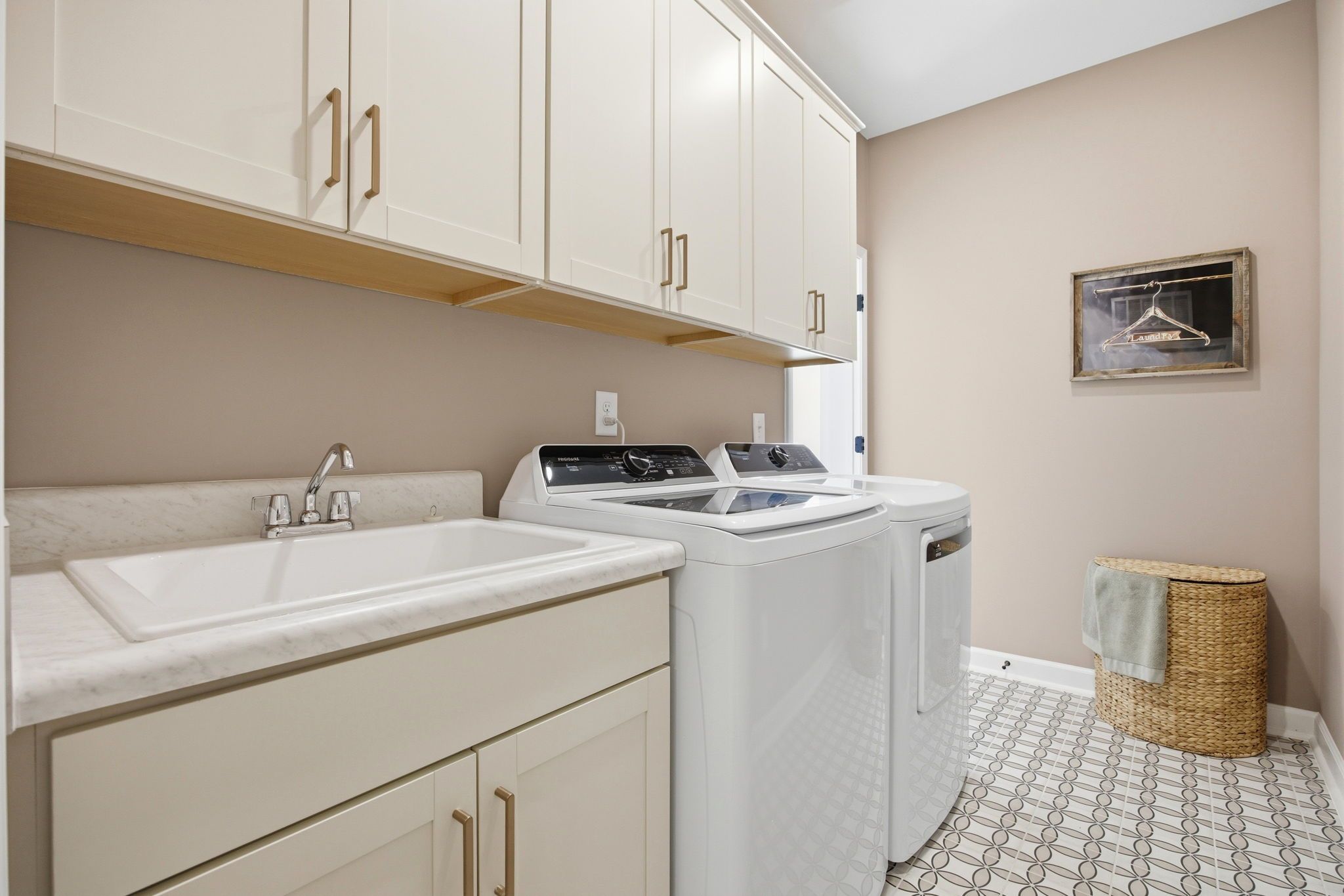 Laundry room in The Ashport featuring built-in cabinets, utility sink, and patterned tile flooring in Wendell, NC.