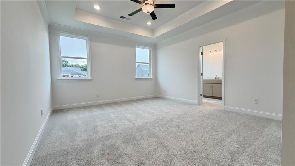 Spacious primary bedroom with tray ceiling and ceiling fan in The Glenwood A floor plan at Wehunt Meadows, Hoschton, GA.