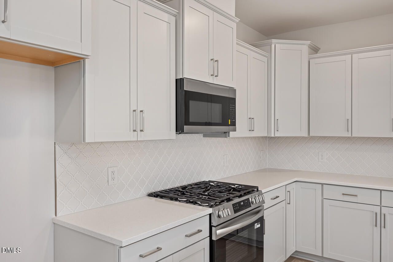 Modern white shaker kitchen with stainless steel gas range, microwave, quartz counters, subway tile backsplash in The Daphne C, Lillington, NC