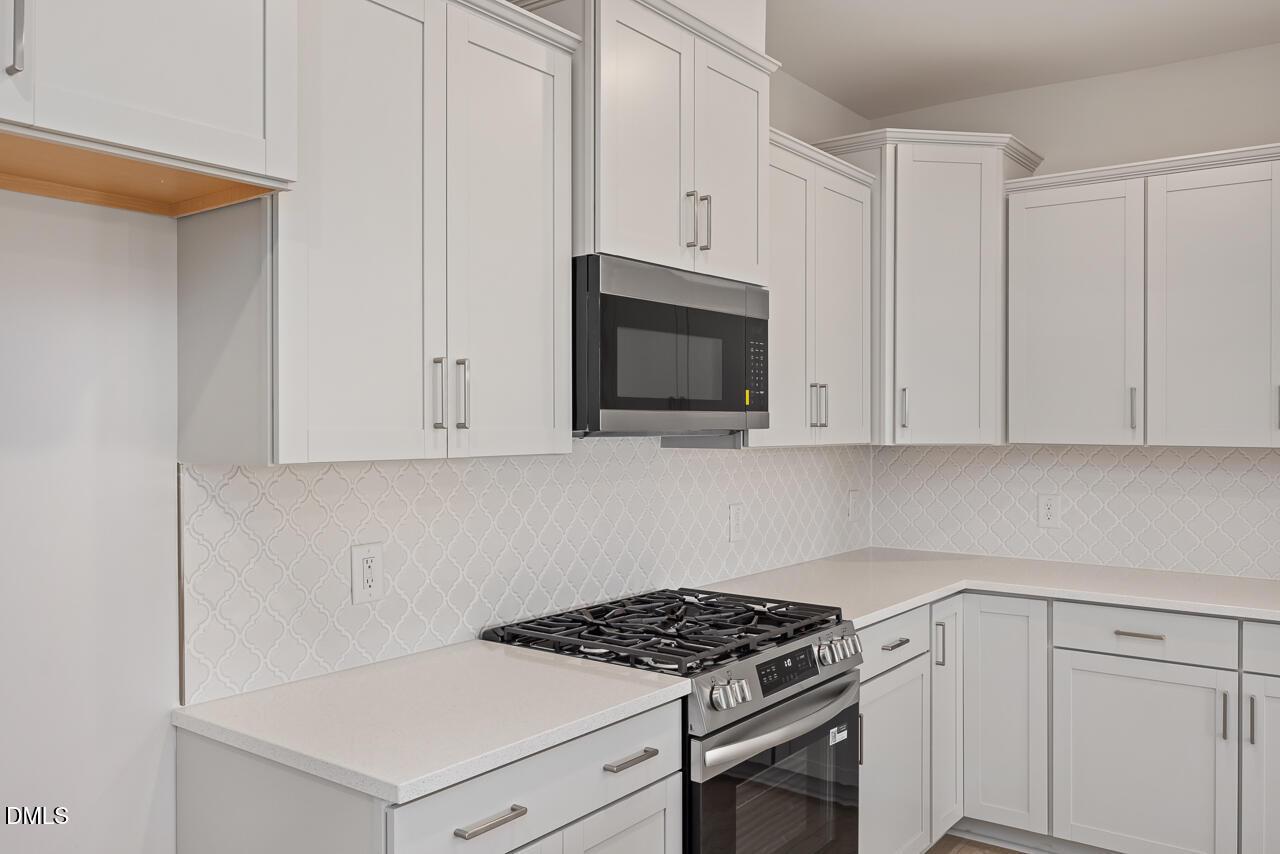Modern white shaker kitchen with stainless steel gas range, microwave, quartz counters, subway tile backsplash in The Daphne C, Lillington, NC