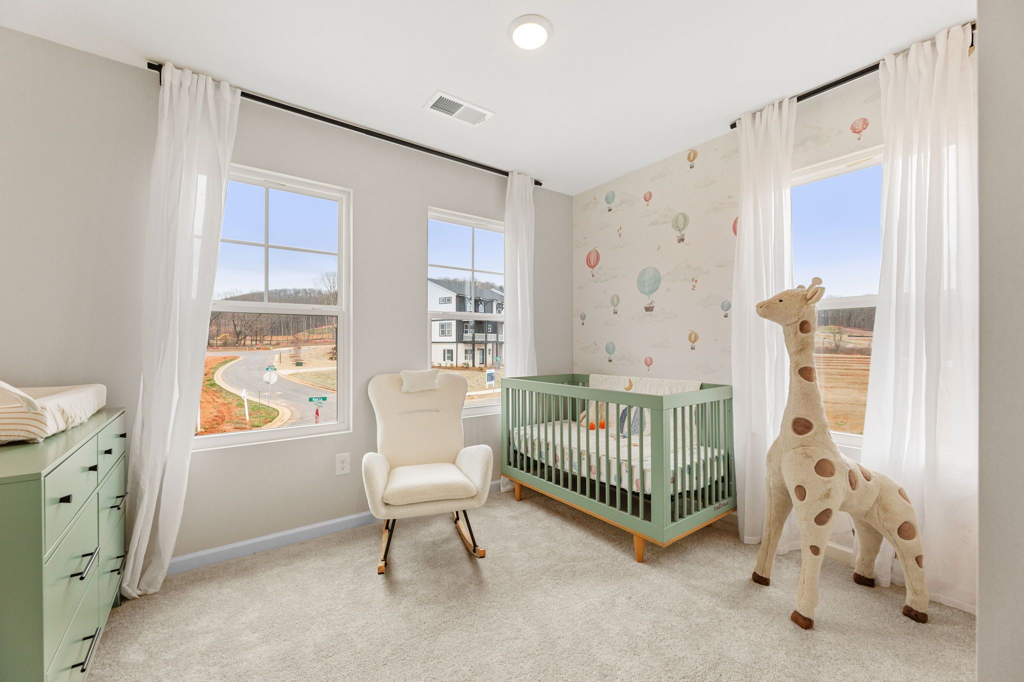 Charming nursery in Hemingway community, Cumming GA featuring mint green crib, plush giraffe, rocking chair and balloon wallpaper