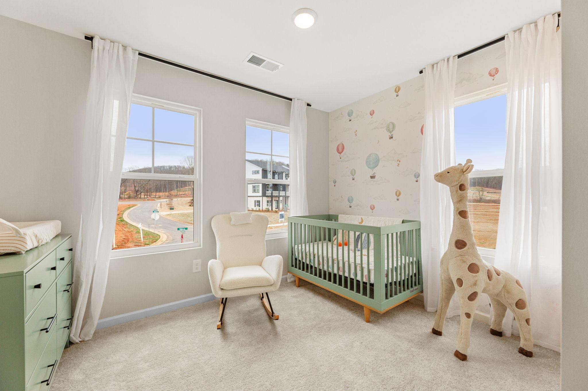 Charming nursery with mint green crib, white rocking chair, stuffed giraffe, and balloon wallpaper in Davidson Homes The Durham B, Cumming, Georgia