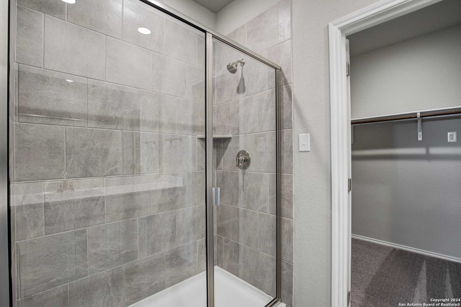 Modern frameless glass shower with gray subway tiles and niche in master bath of Davidson Homes The Blanco C, San Antonio