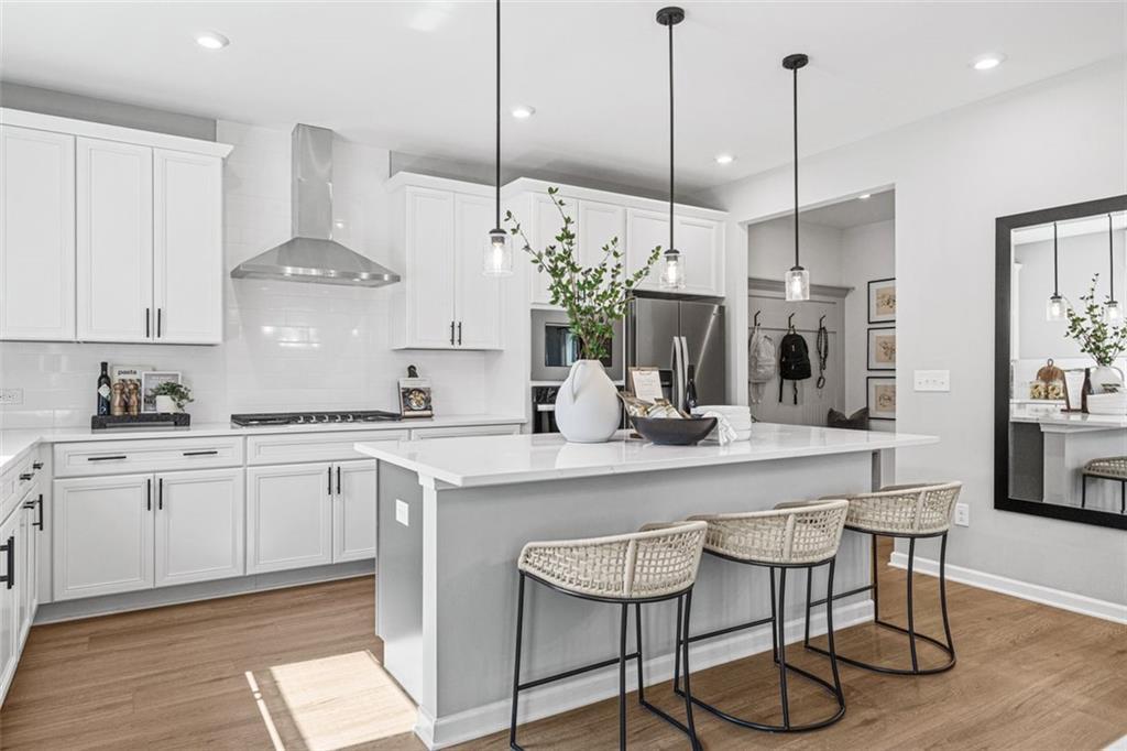 Modern white kitchen with stainless appliances, large island, bar stools, and pendant lights in Davidson Homes The Hickory B, Hoschton, GA