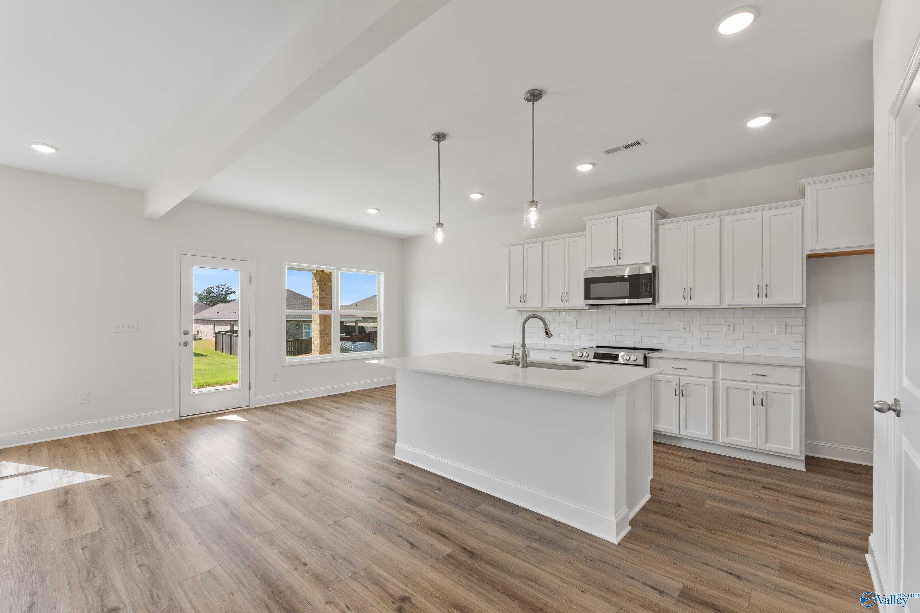 Modern open kitchen with white island, cabinets, pendant lights, and backyard view in Davidson Homes Shelby A, New Market AL