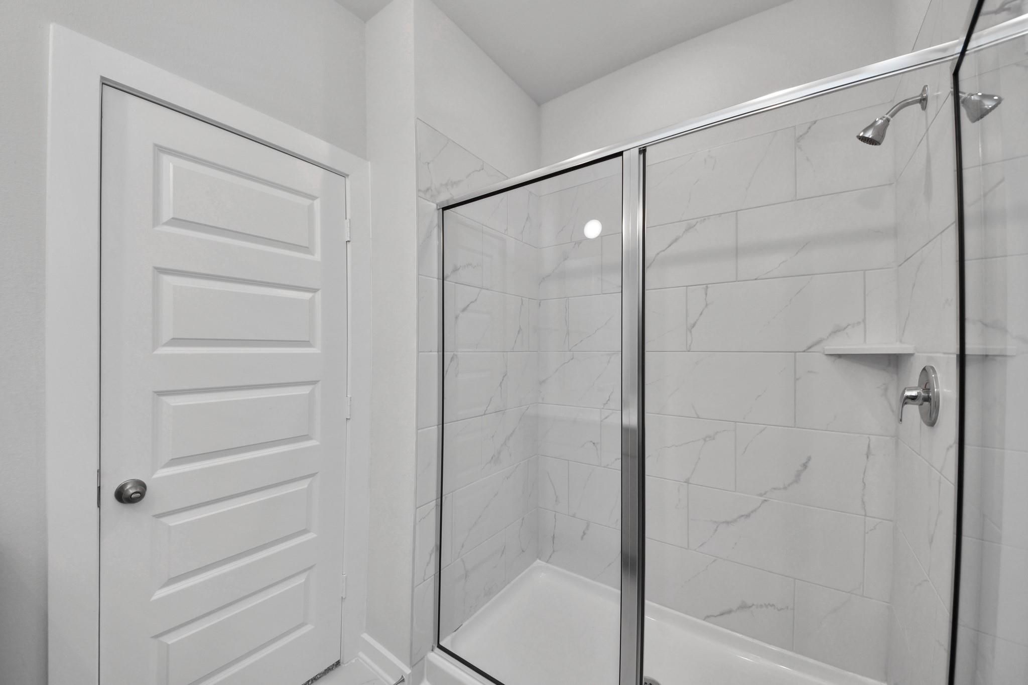 Walk-in shower with white marble-look tile and glass door in The Colorado G floor plan at Emberly, Beasley, Texas.