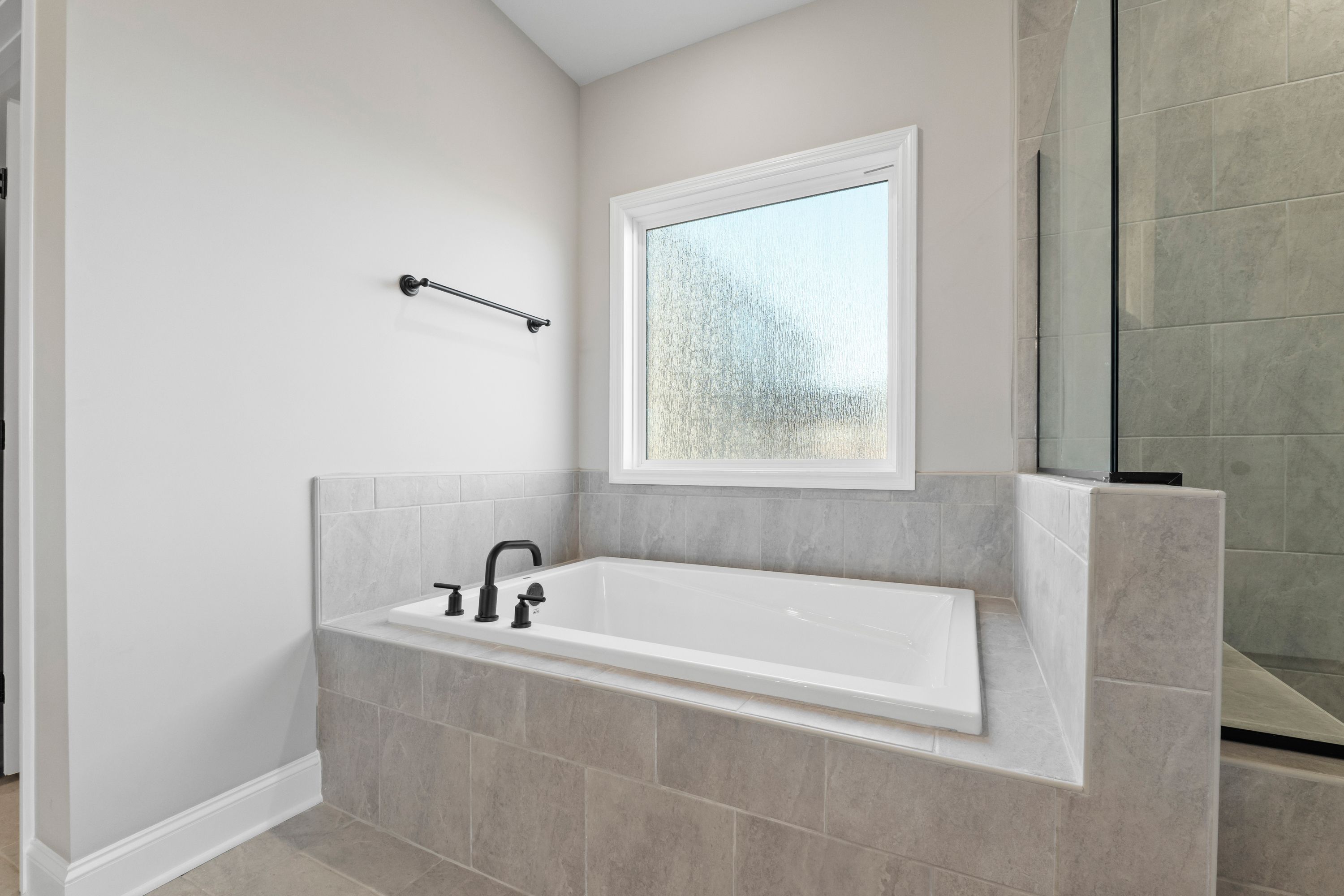 Luxurious master bathroom in The Valencia with freestanding tub, gray tile surround, glass shower, and frosted window