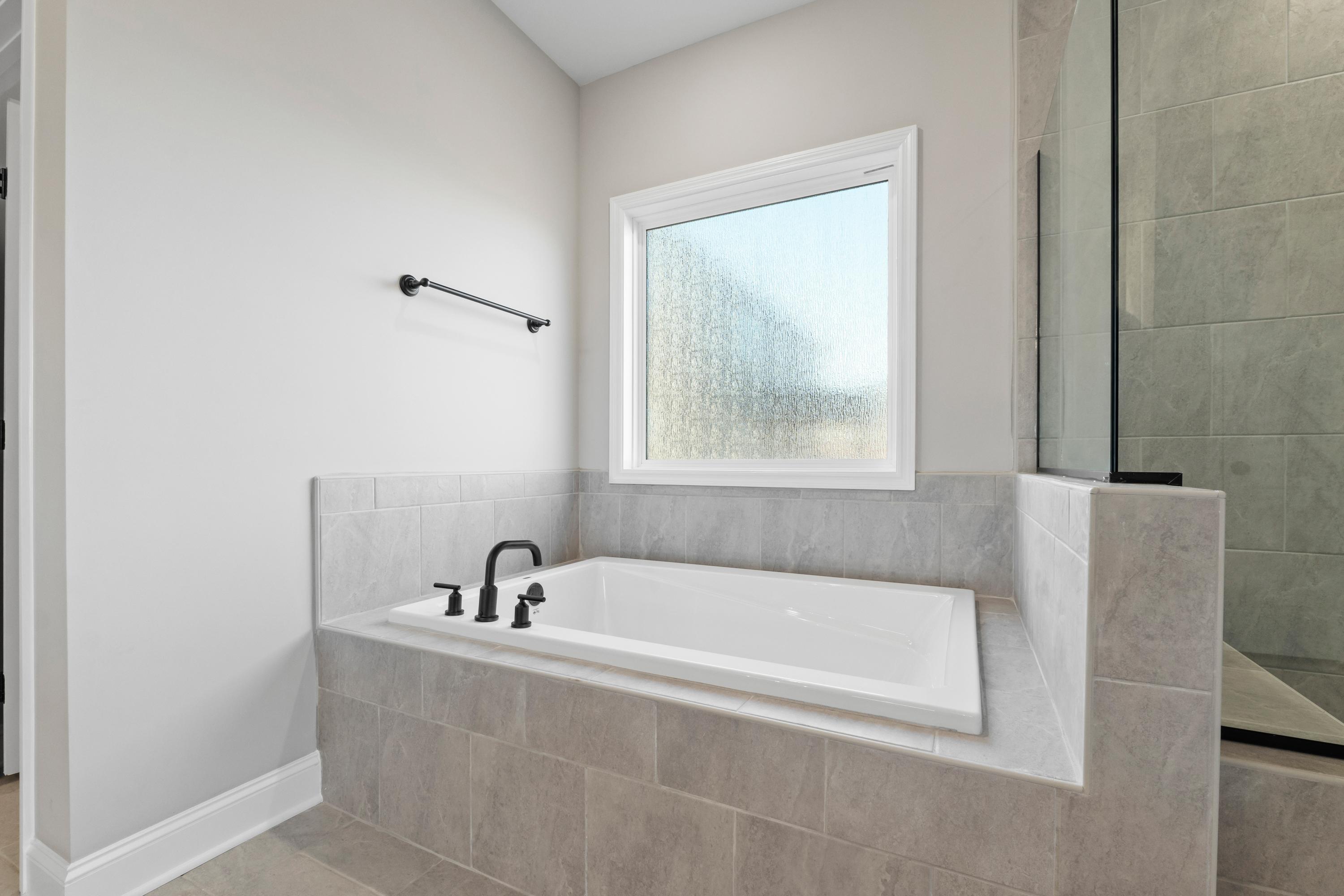 Luxurious master bathroom in The Valencia with freestanding tub, gray tile surround, glass shower, and frosted window