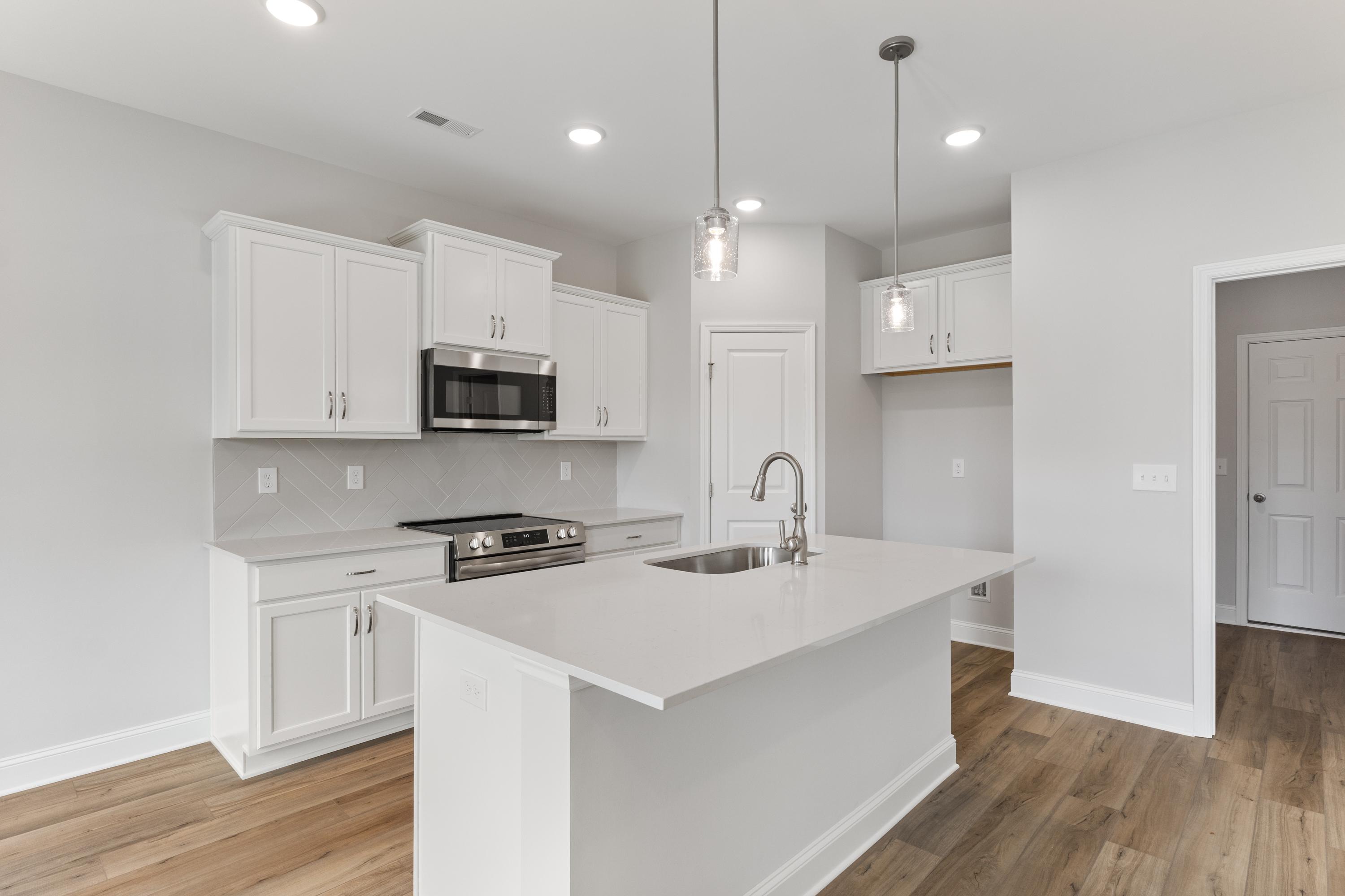 Modern kitchen in The Butler by Davidson Homes featuring white cabinets, stainless steel appliances, and large island sink