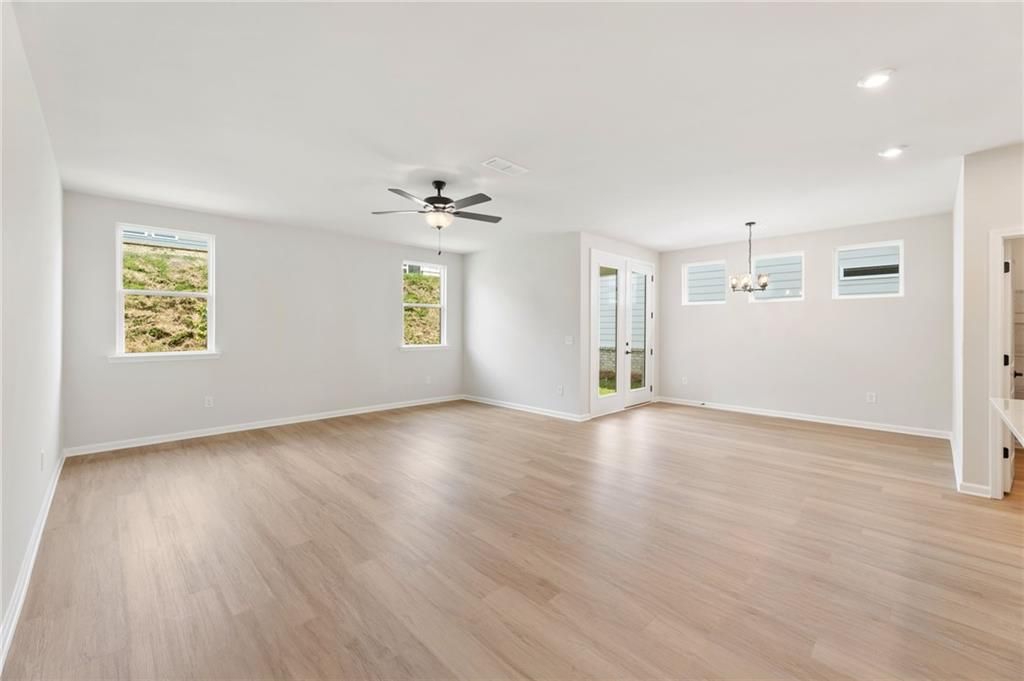 Bright open living room with light hardwood floors, large windows, ceiling fan, chandelier, and French doors in Davidson Homes The Daphne C, Loganville, GA