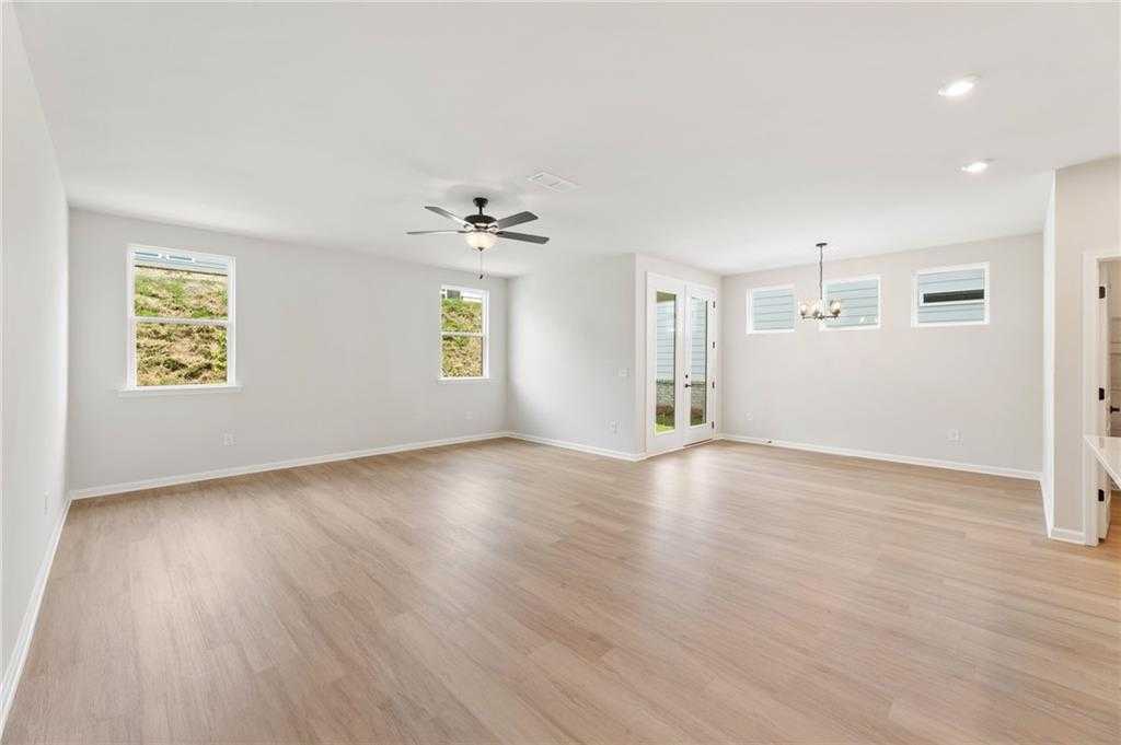 Open great room with large windows, ceiling fan, glass French doors, and hardwood floors in Davidson Homes The Daphne C, Loganville, GA