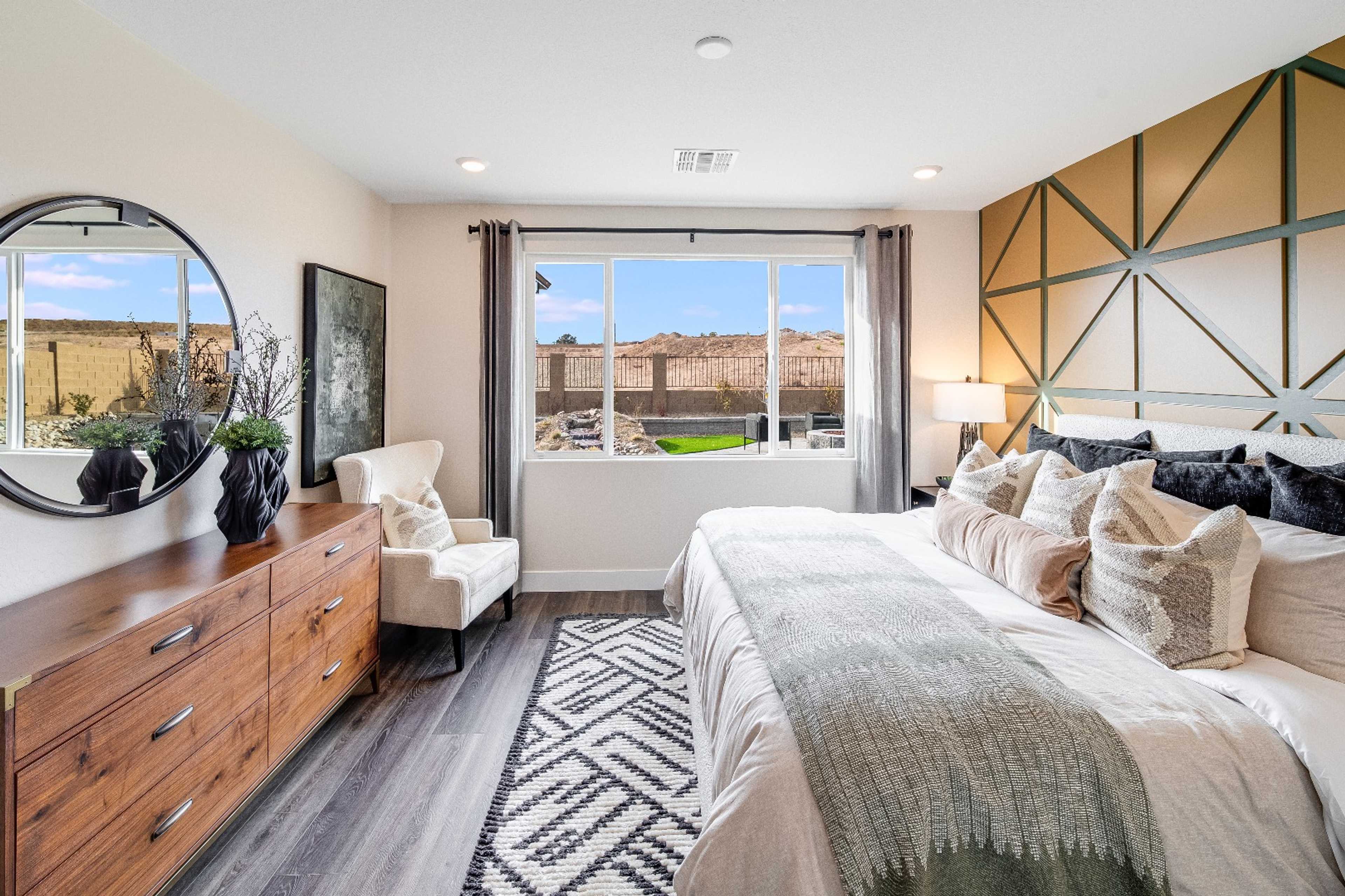 Spacious master bedroom at South Ranch Western Collection in Prescott AZ with geometric accent wall, king bed, large scenic windows, hardwood floors, wooden dresser