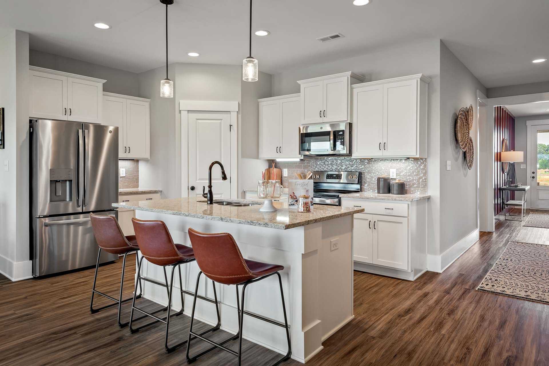 Spacious modern kitchen at Heritage Lakes in New Market Alabama with white cabinets, granite island, leather bar stools, and hardwood floors