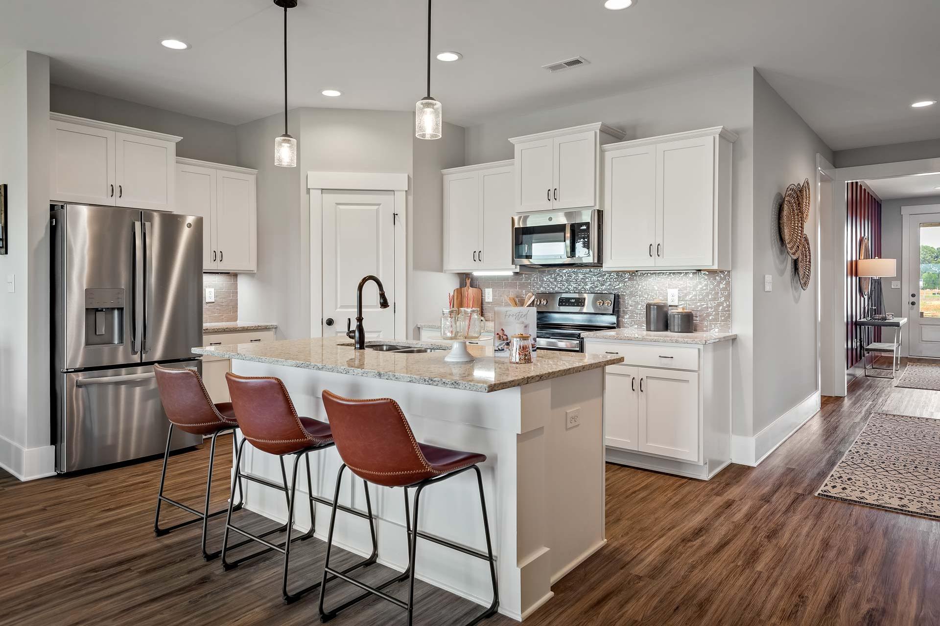 Spacious modern kitchen at Heritage Lakes in New Market Alabama with white cabinets, granite island, leather bar stools, and hardwood floors