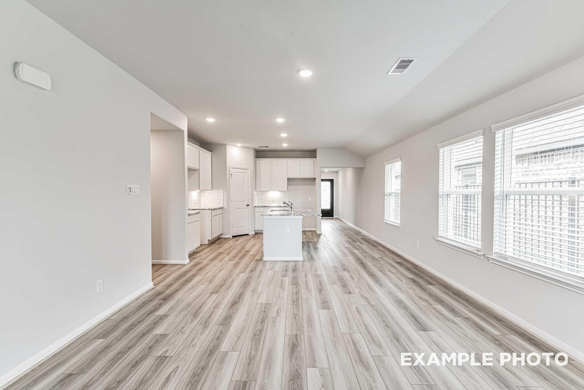 Spacious open-concept living and kitchen with white cabinetry, central island, hardwood floors, and large windows in Davidson Homes Riviera A, Rosharon, Texas