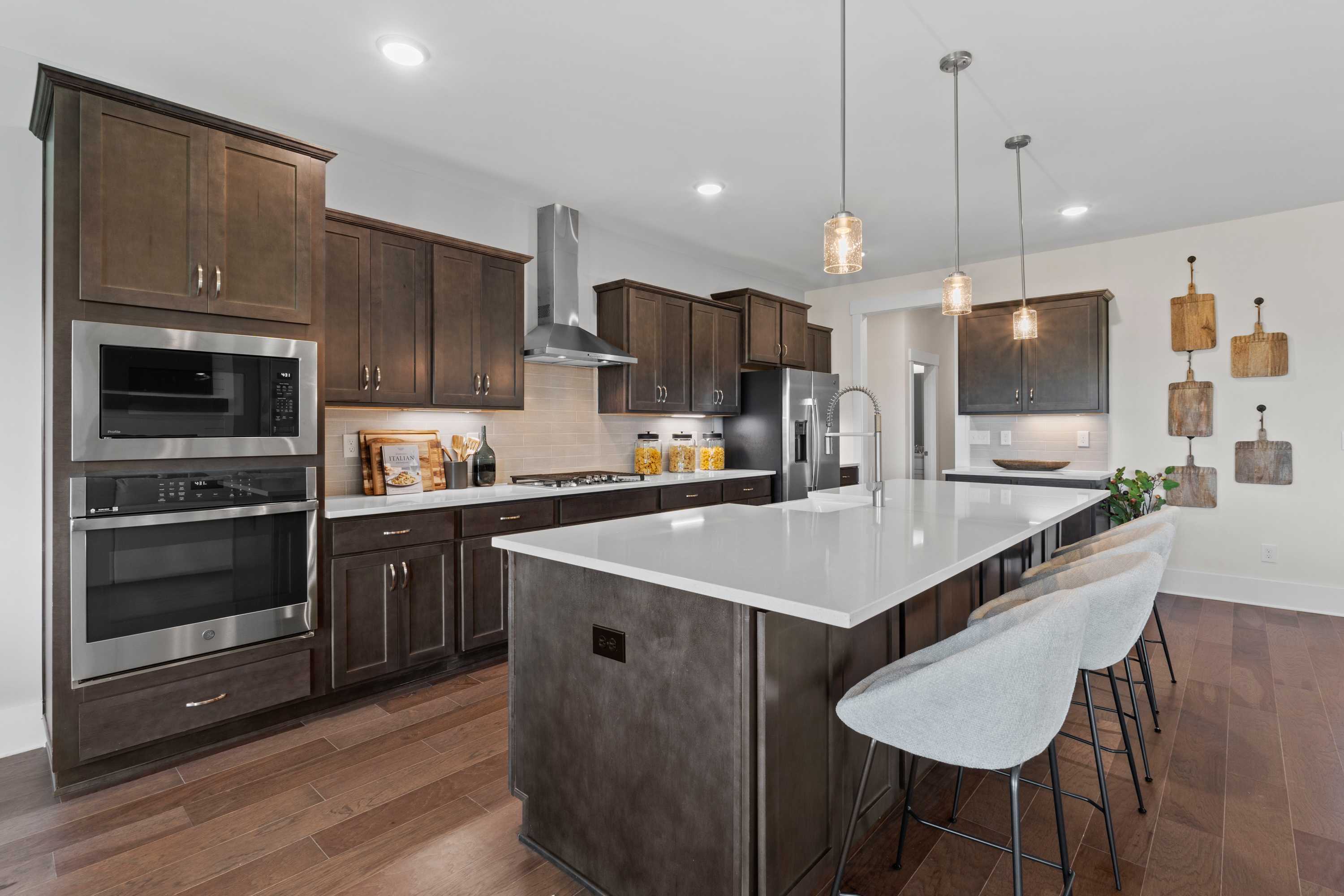 Modern kitchen in Creekside, Harvest AL with dark wood cabinets, white quartz island, stainless appliances, and hardwood floors