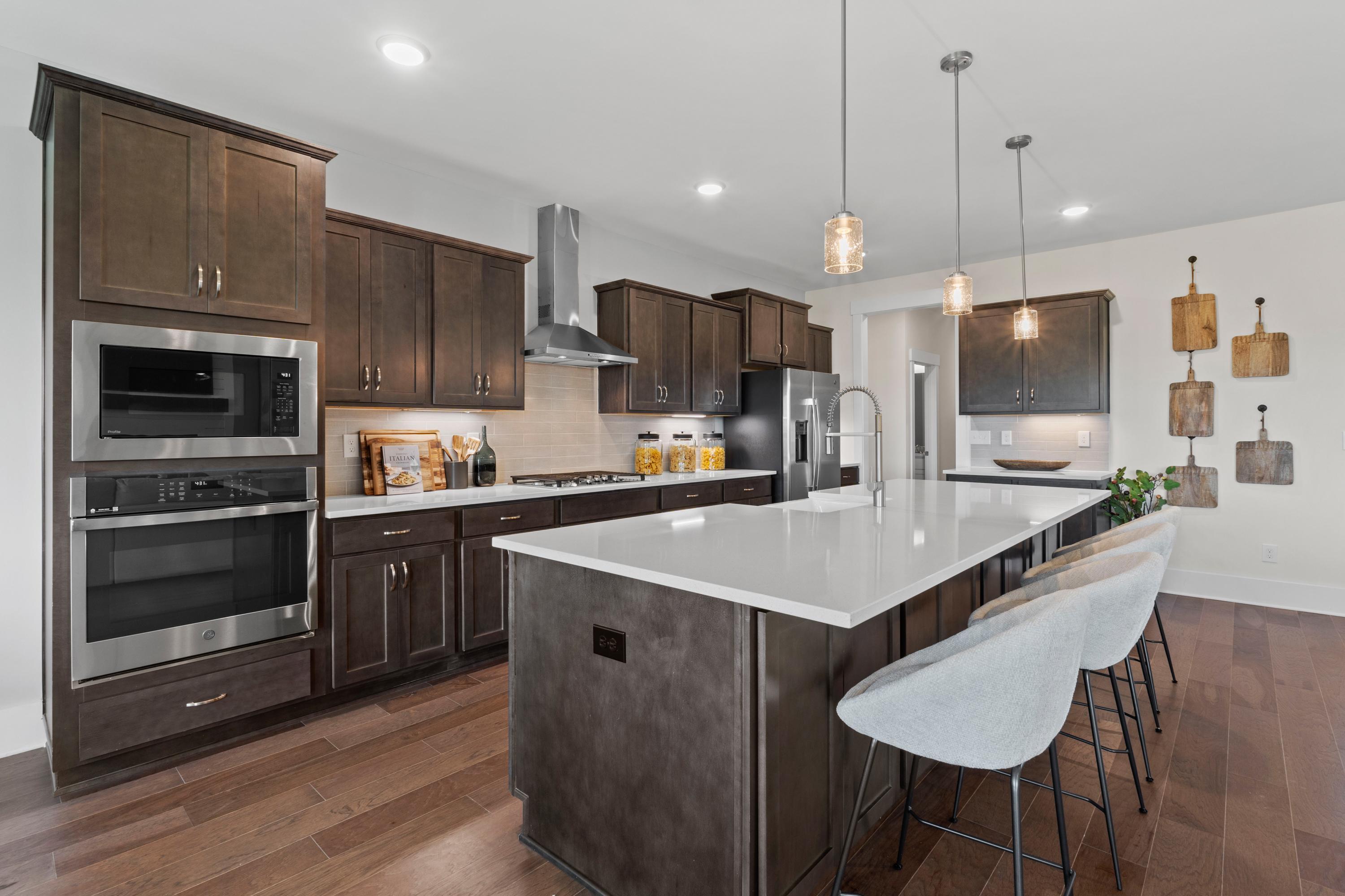 Modern kitchen in Creekside, Harvest AL with dark wood cabinets, white quartz island, stainless appliances, and hardwood floors