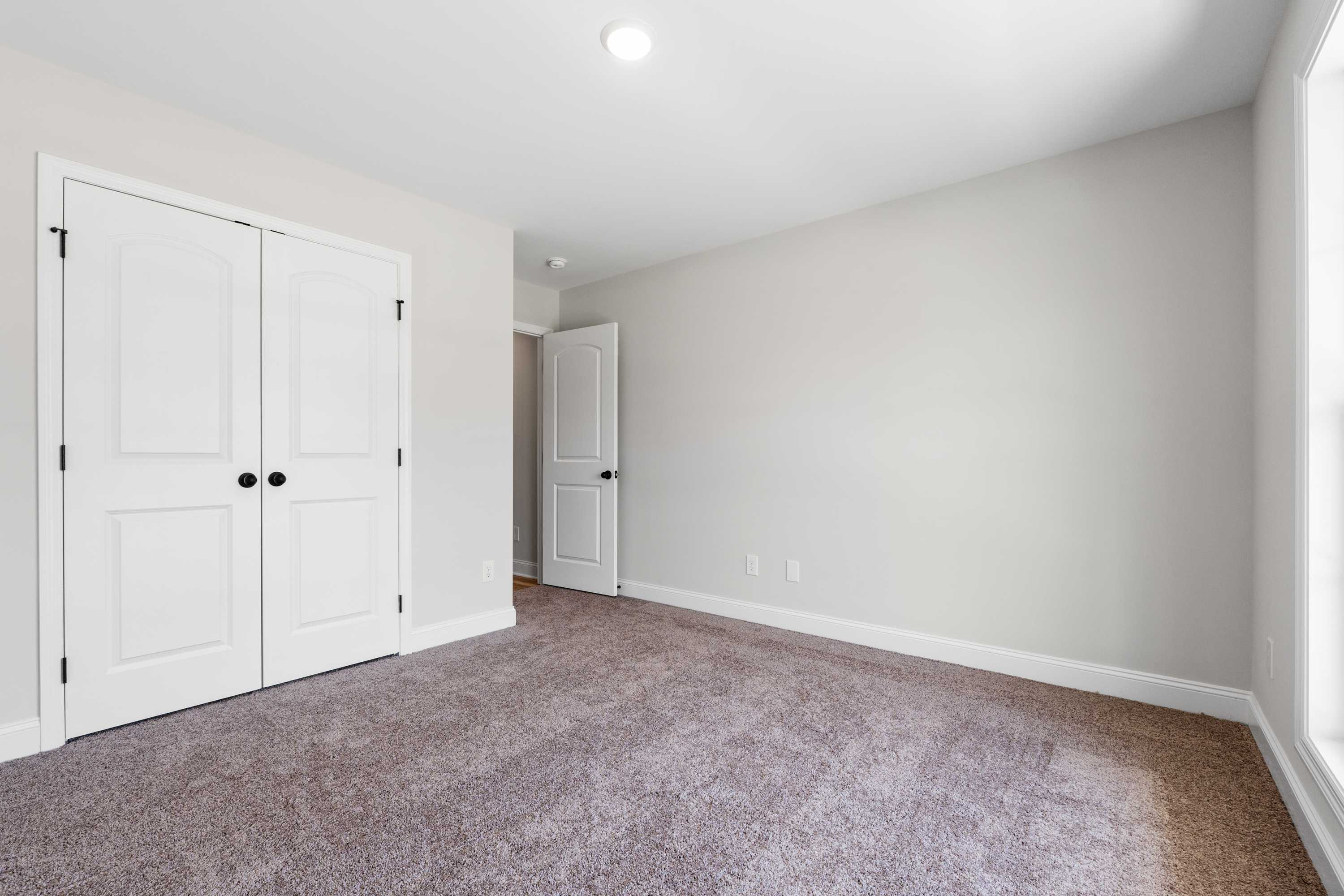 Spacious secondary bedroom in The Everett C with beige walls, white bi-fold closet doors, en-suite bath access, large window, and neutral carpet