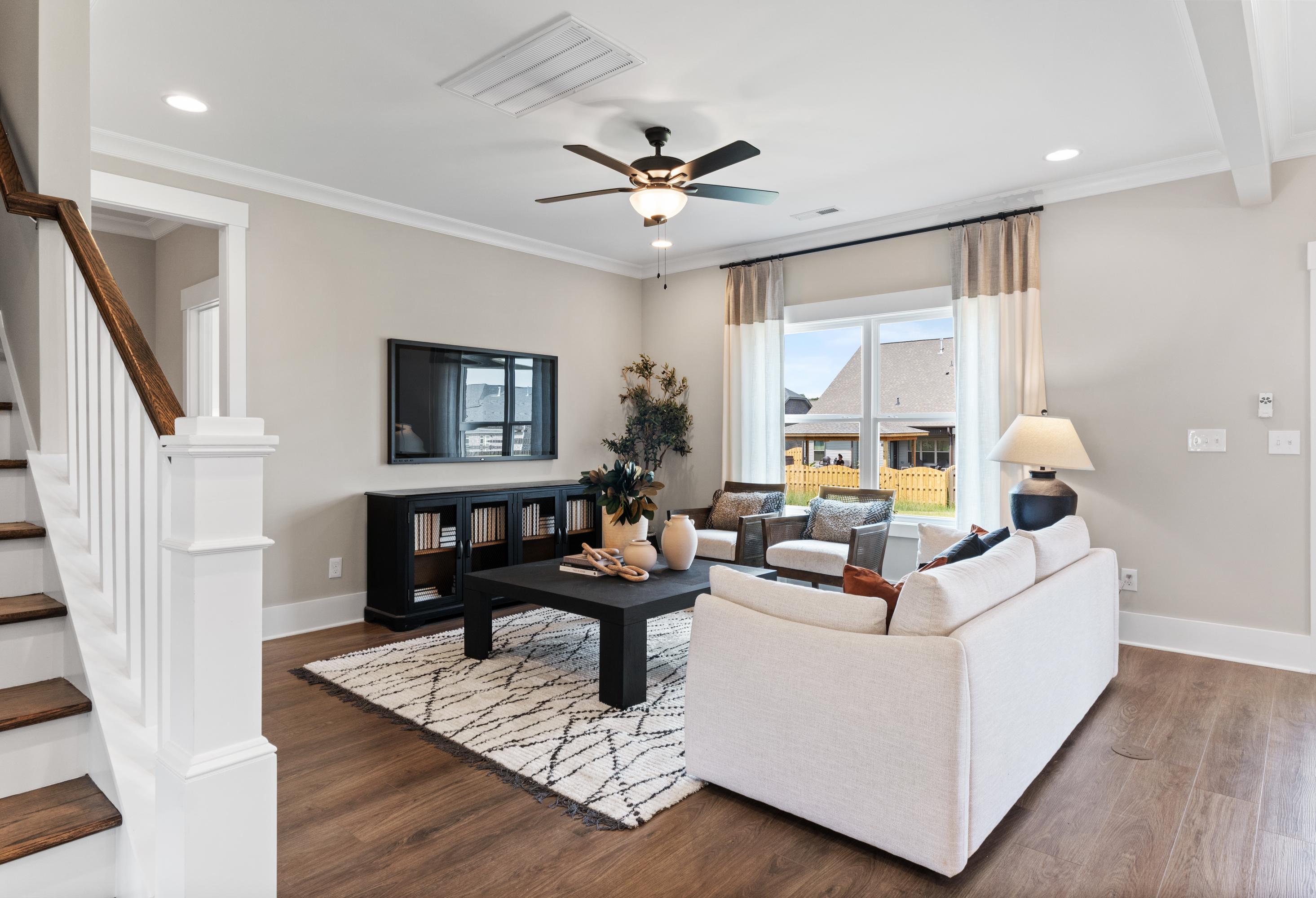 Spacious living room in Shelby B home with white sofa, black coffee table, ceiling fan, and open wooden staircase