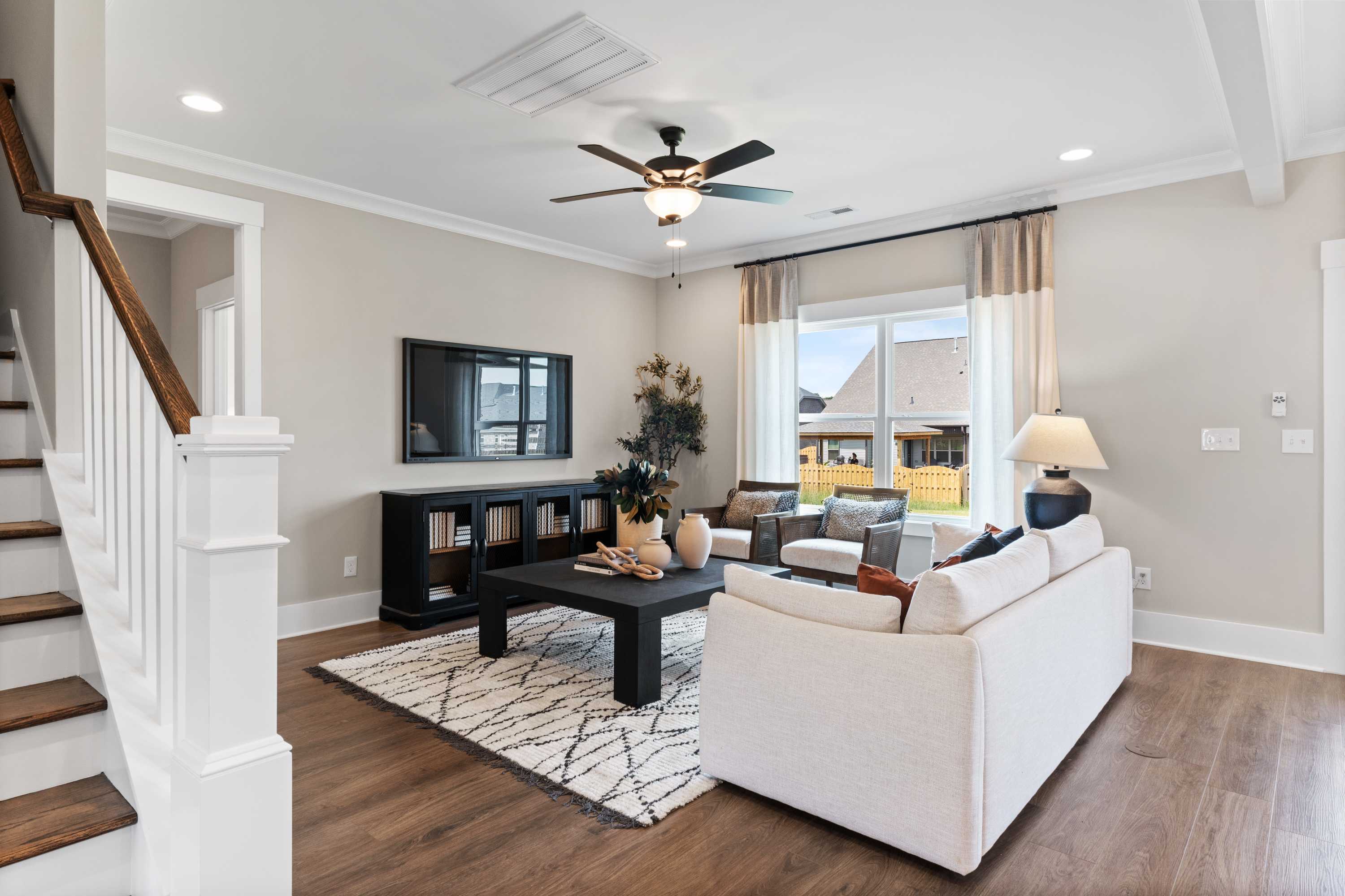 Spacious living room in Shelby B home with white sofa, black coffee table, ceiling fan, and open wooden staircase