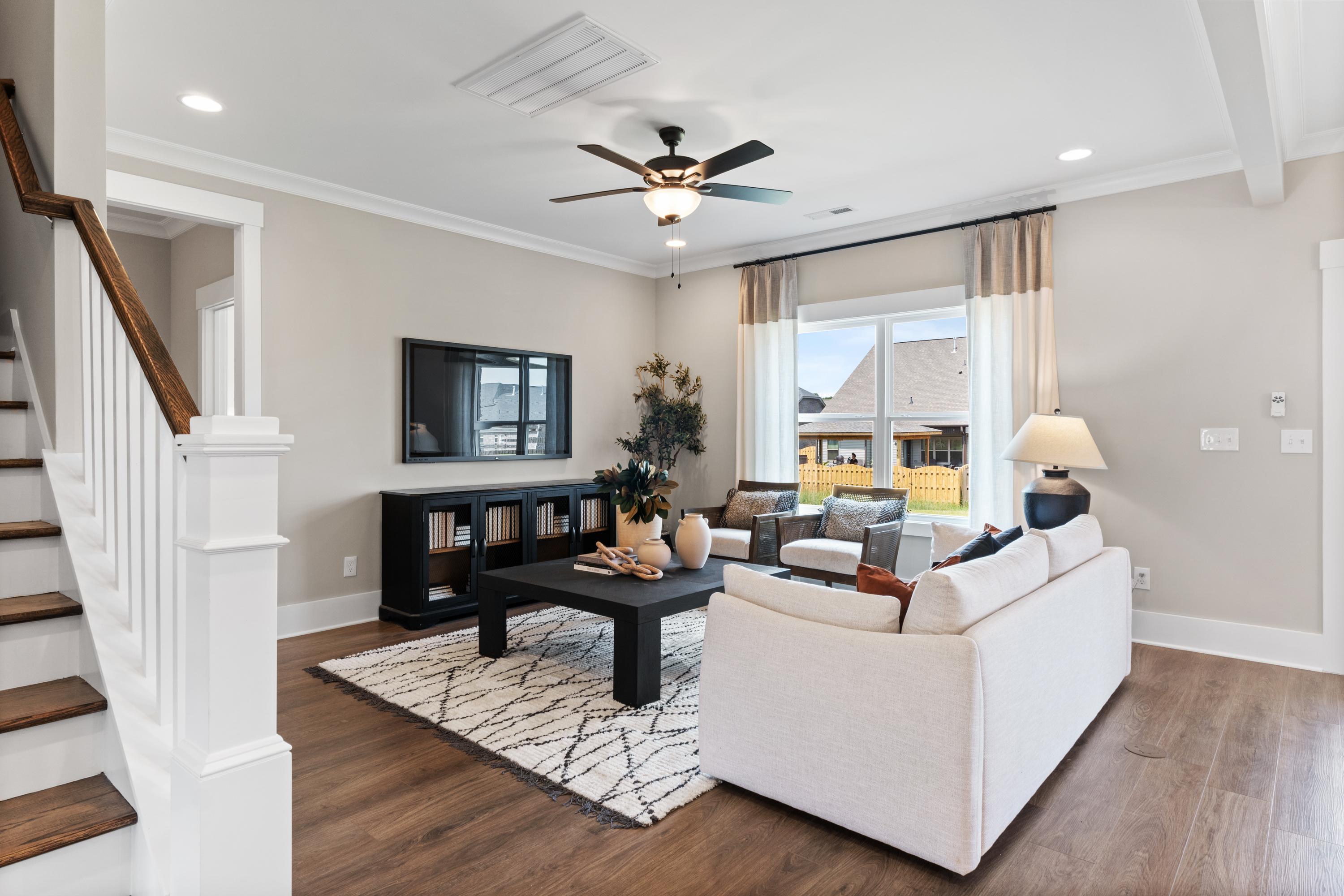 Spacious living room in Shelby B home with white sofa, black coffee table, ceiling fan, and open wooden staircase