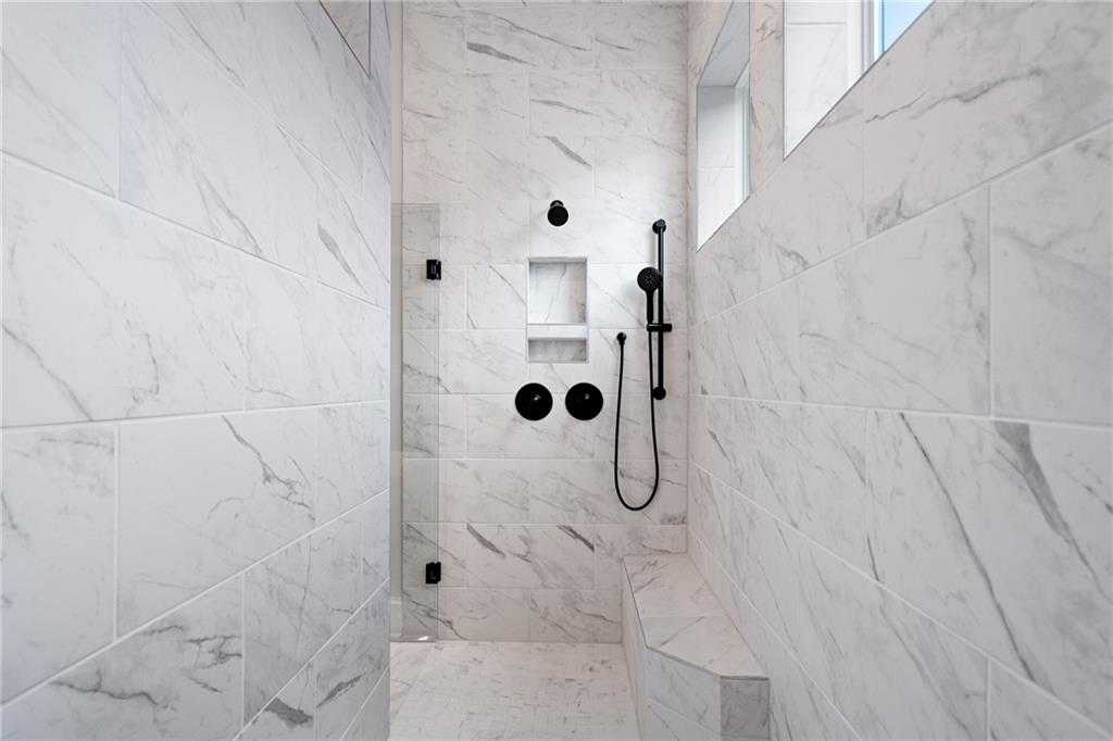Elegant walk-in marble shower with black fixtures, glass enclosure, and bench in Davidson Homes Seaside B master bath, Woodstock, GA