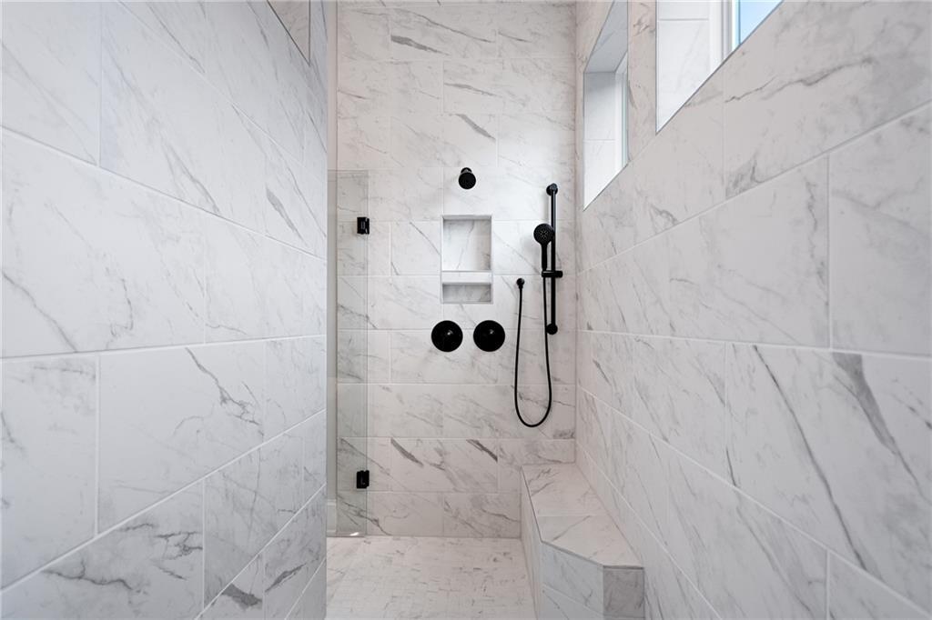 Elegant walk-in marble shower with black fixtures, glass enclosure, and bench in Davidson Homes Seaside B master bath, Woodstock, GA