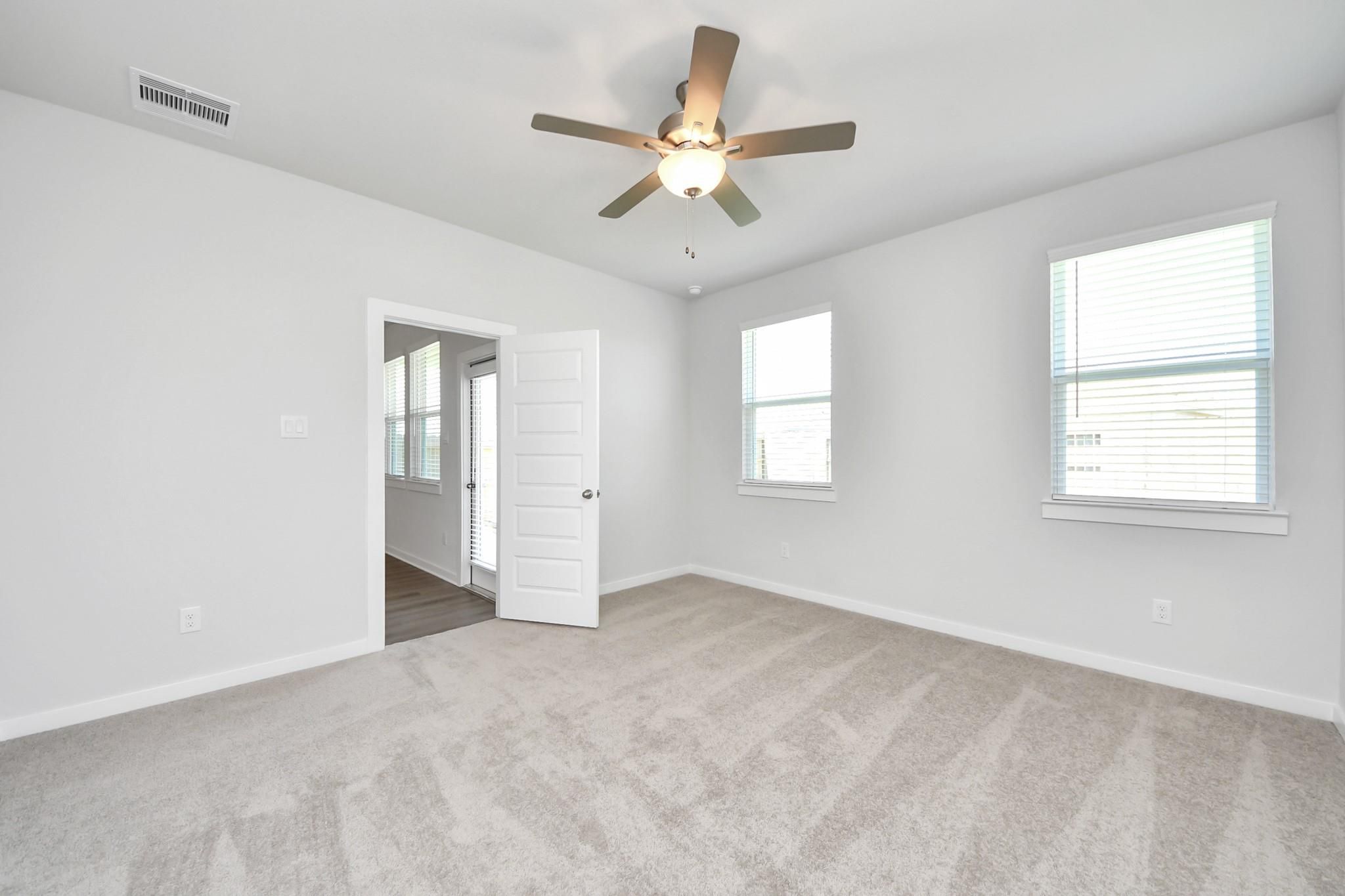 Bright empty bedroom with carpet, ceiling fan, and windows in Davidson Homes' The Costa A plan, Emberly, Beasley, TX