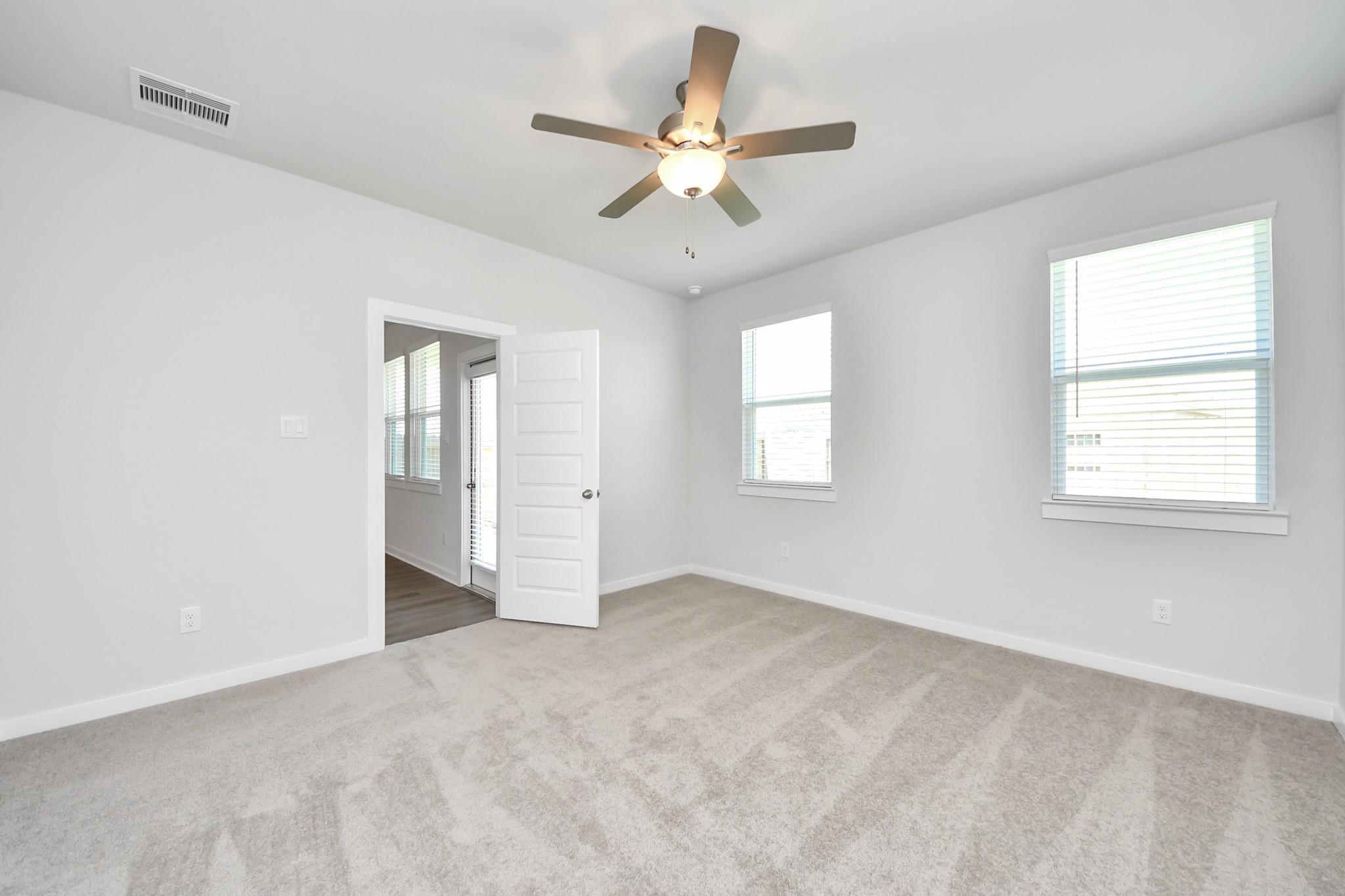 Bright empty bedroom with carpet, ceiling fan, and windows in Davidson Homes' The Costa A plan, Emberly, Beasley, TX