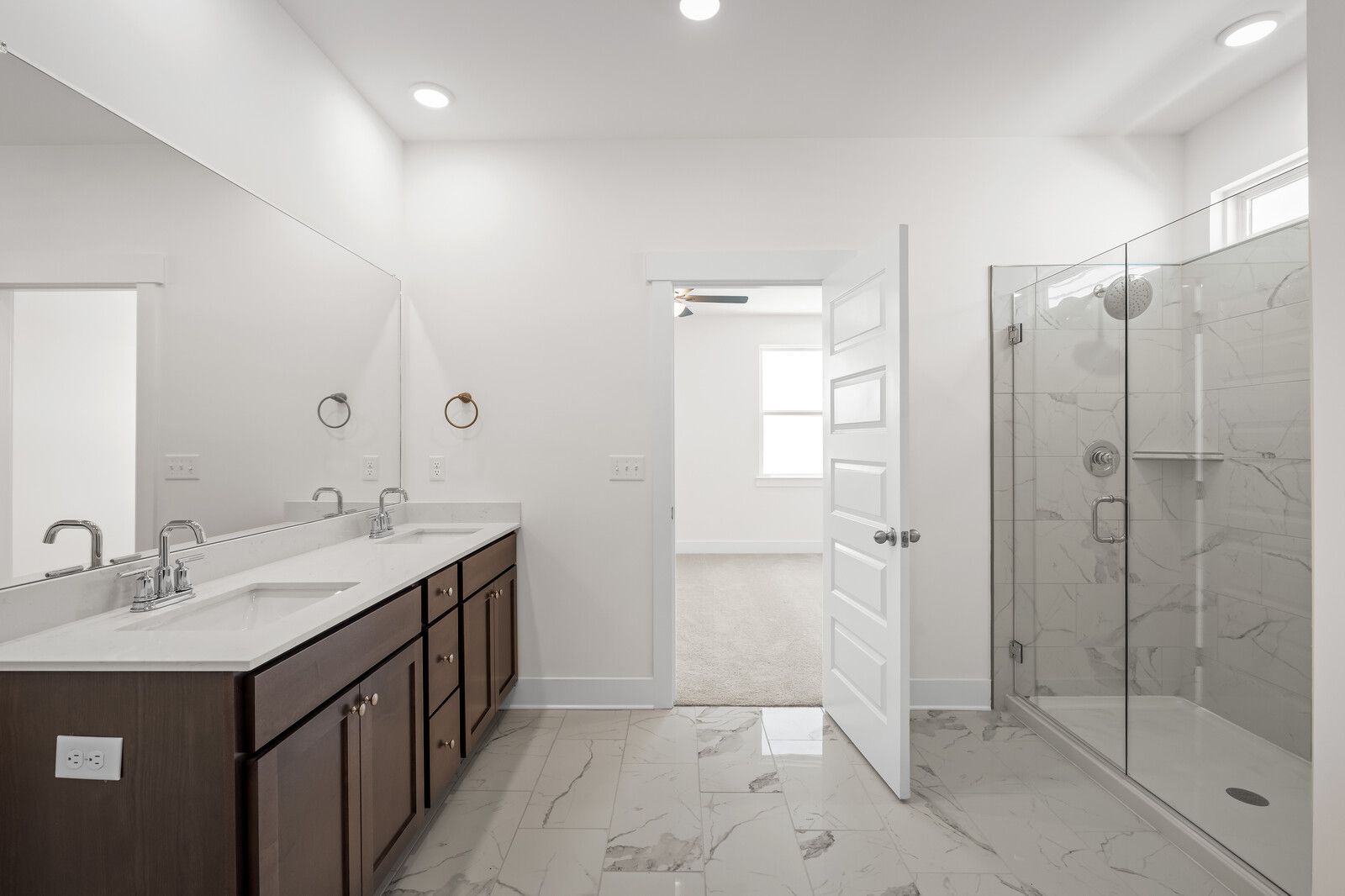 Master bathroom in The Cottonwood featuring a dual-sink vanity, marble-style flooring, and a glass-enclosed shower.