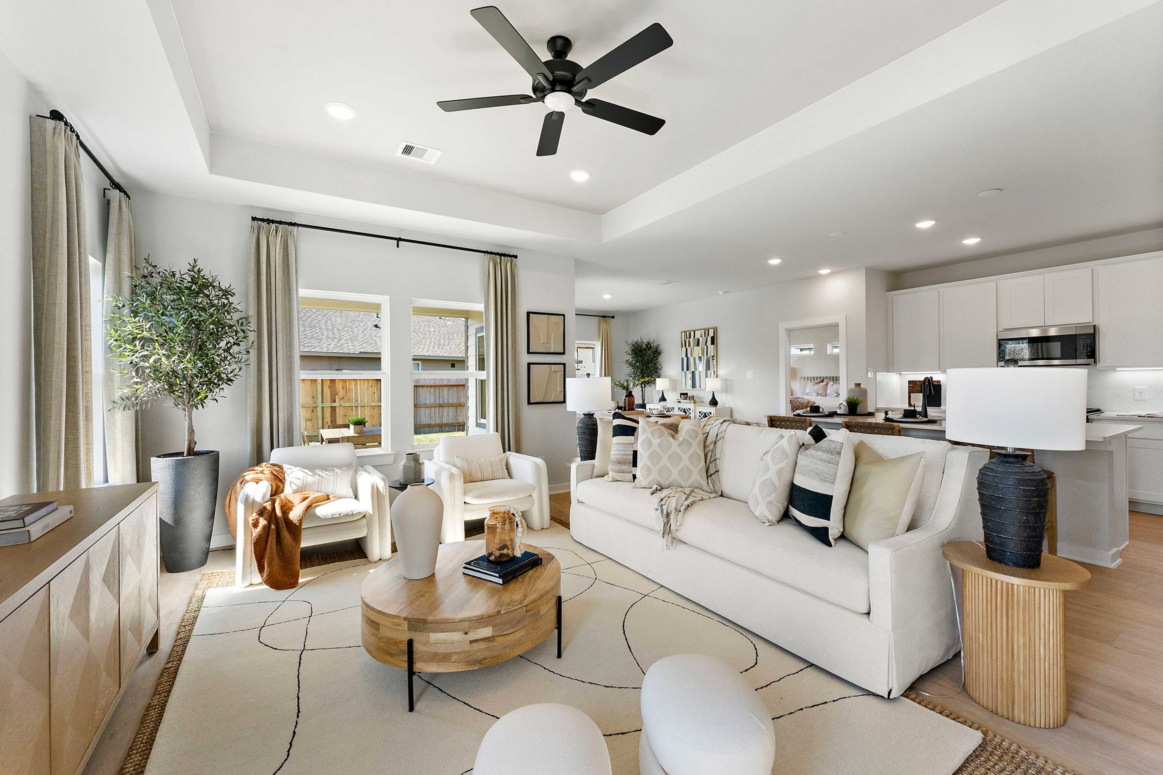 Spacious open-concept living room in Sundance Cove, Crosby Texas by Davidson Homes with white sofa, wooden coffee table, potted plants, and modern kitchen