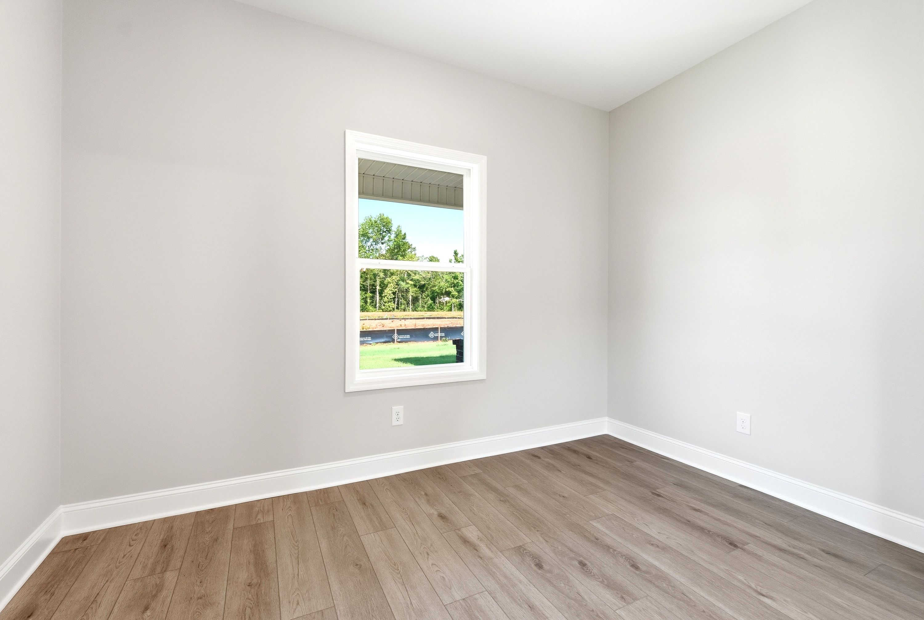 Bright, neutral bedroom in The Russell A floor plan featuring wood-style flooring and a single window with outdoor views.