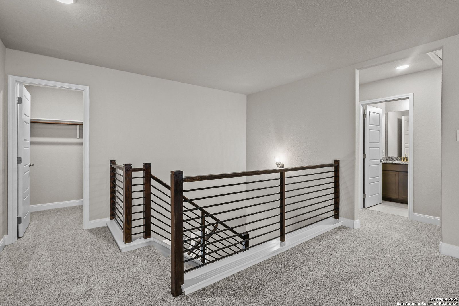 Upstairs hallway with wooden staircase railing, carpeted floor, bedroom closet, and bathroom vanity in Davidson Homes The Jennings G, Castroville, Texas