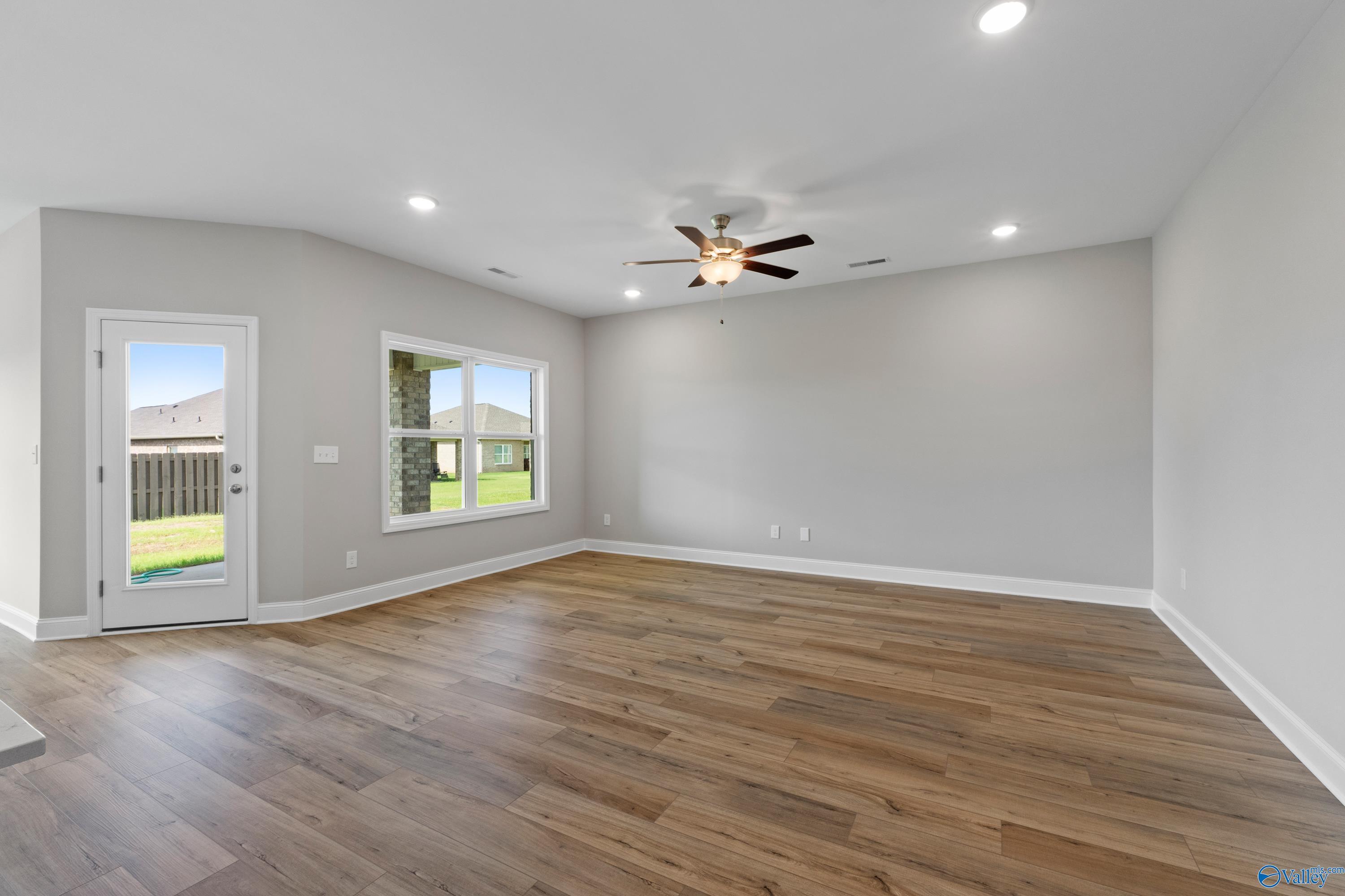 Bright living room with hardwood floors, ceiling fan, large windows, and backyard view in Everett B floor plan, Ivy Hills, Toney, Alabama