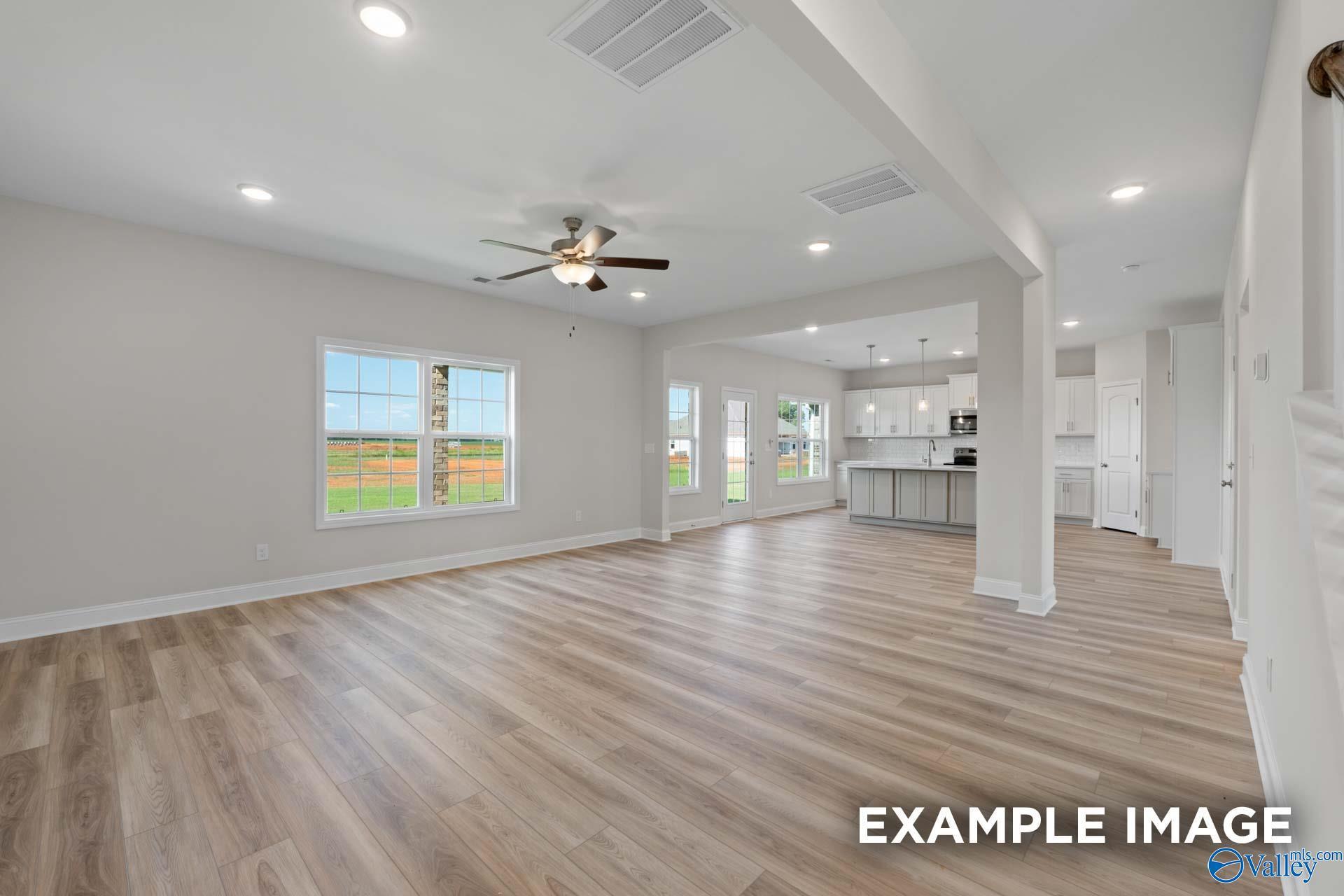 Bright open living area with luxury vinyl plank floors, ceiling fan, and large windows overlooking fields in 5-bedroom Madison A home, Toney, AL