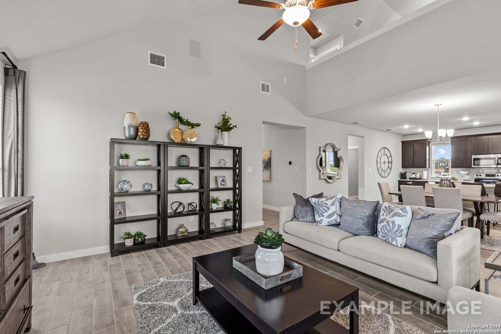 Spacious open-concept living room with vaulted ceiling, ceiling fan, wooden shelves, and modern sofa in The Collin A, Seguin, Texas