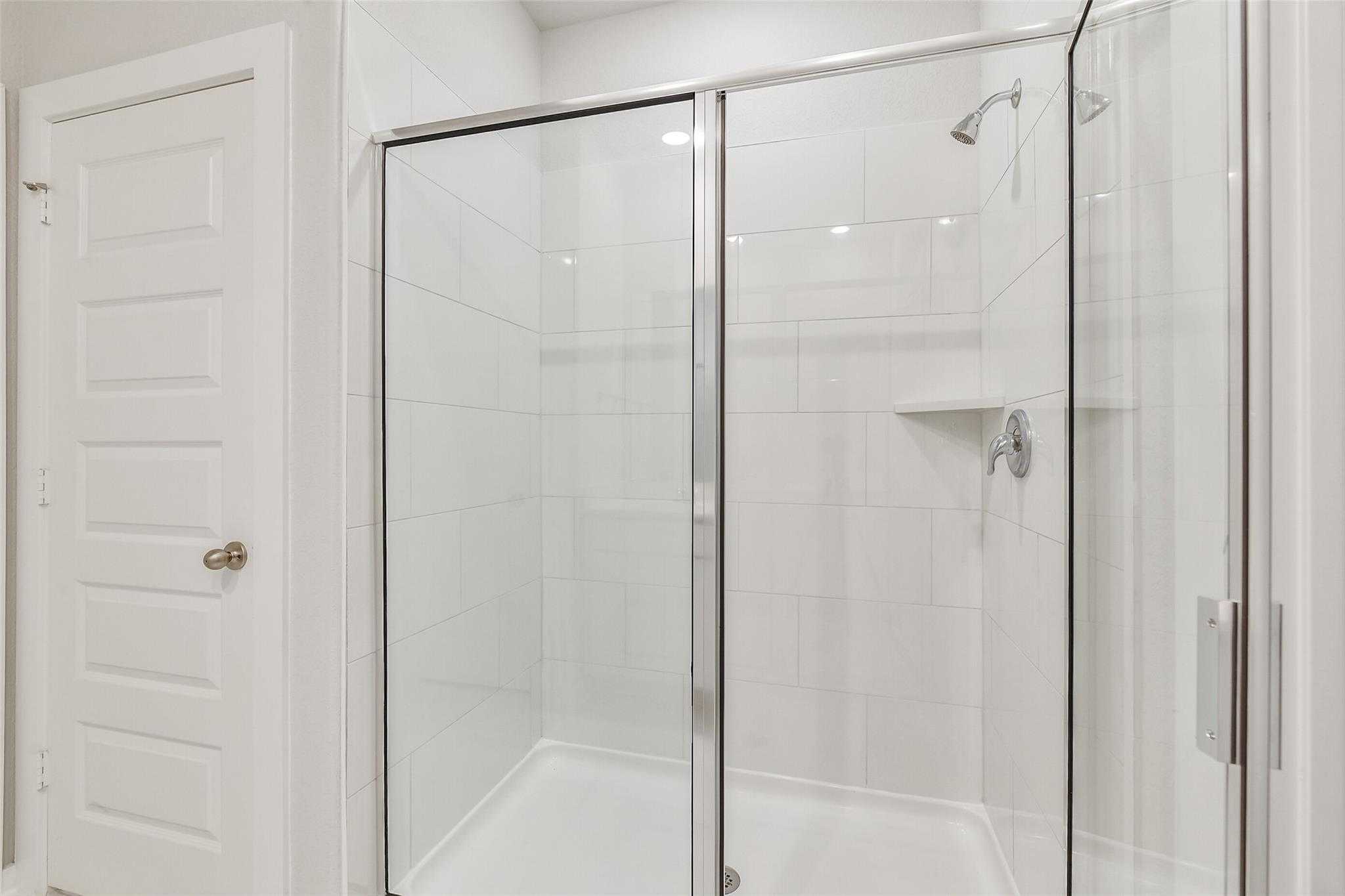 Modern frameless glass shower with white subway tiles, rainfall head, and niche in The Blanco E master bath, Davidson Homes, Magnolia, Texas