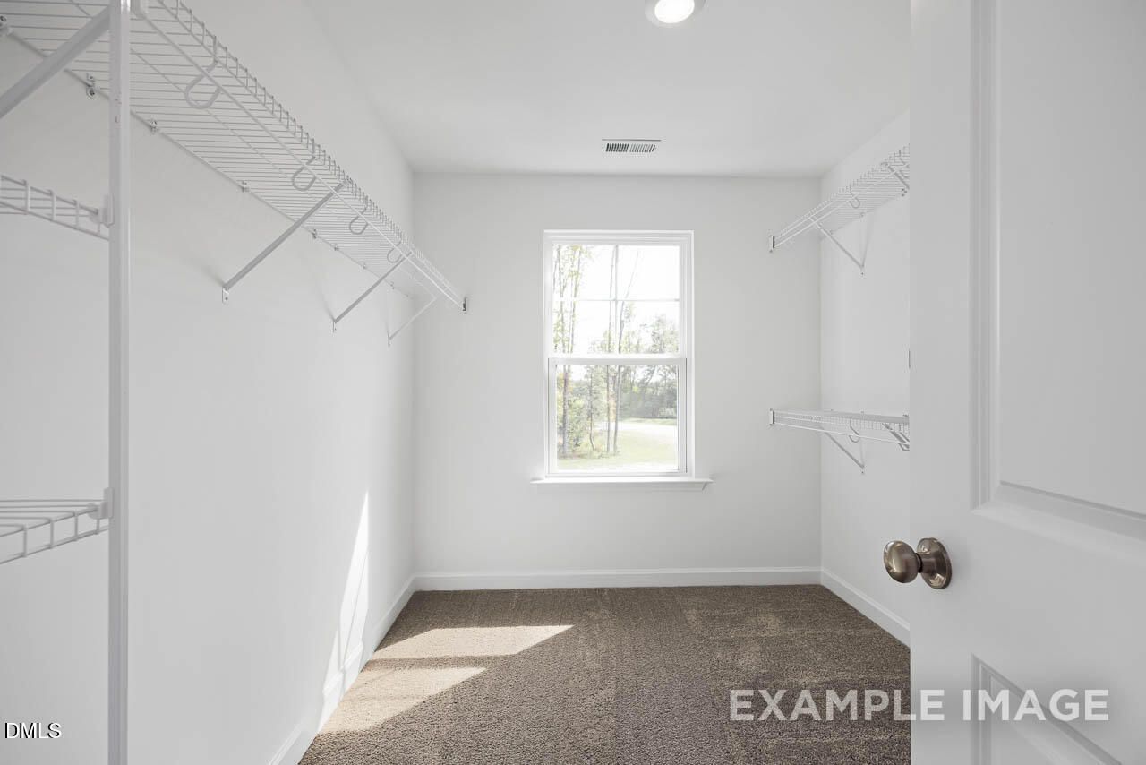 Bright walk-in closet with wire shelving, hanging rods, and window in Davidson Homes The Willow D, Zebulon, NC