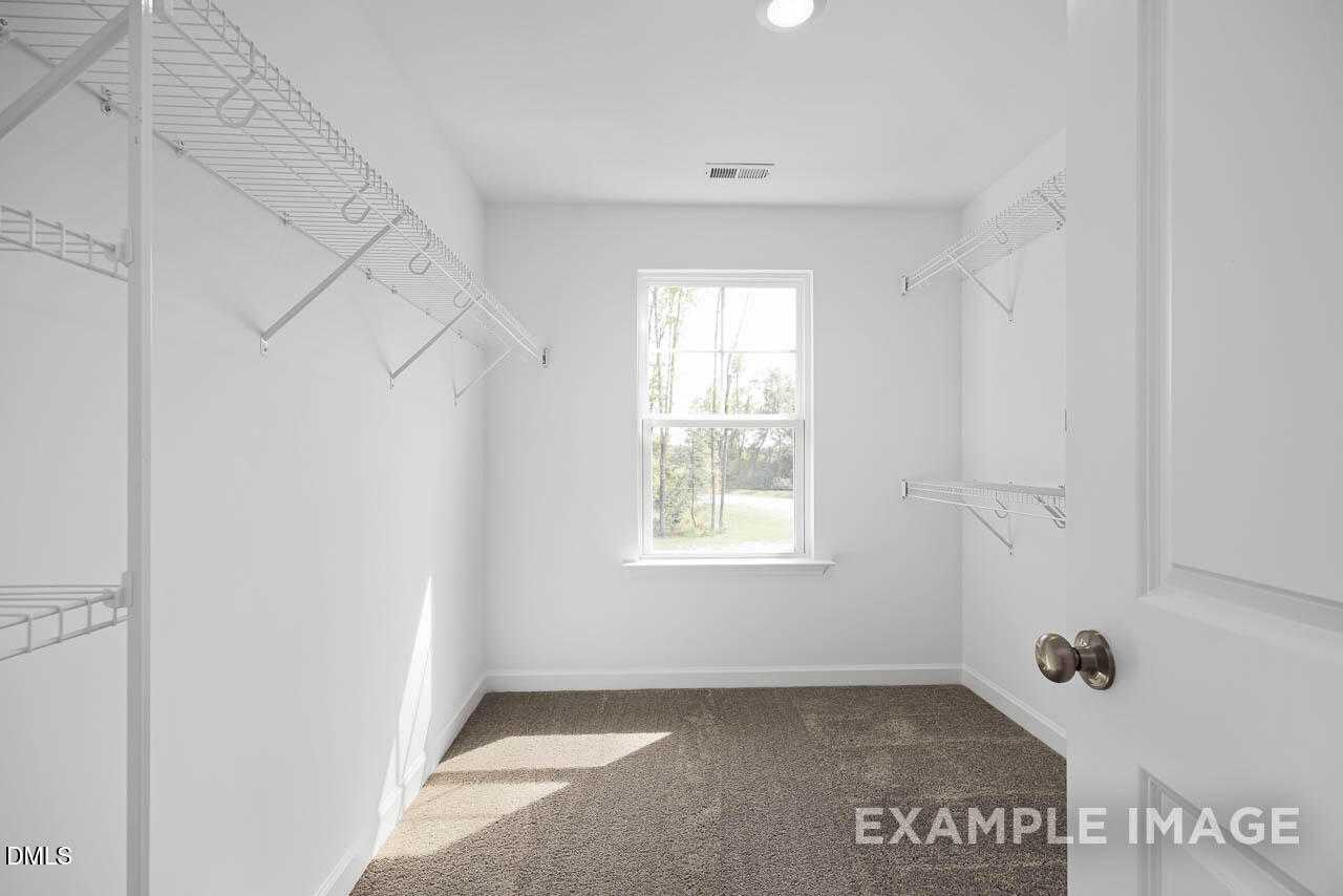 Bright walk-in closet with wire shelving, hanging rods, and window in Davidson Homes The Willow D, Zebulon, NC