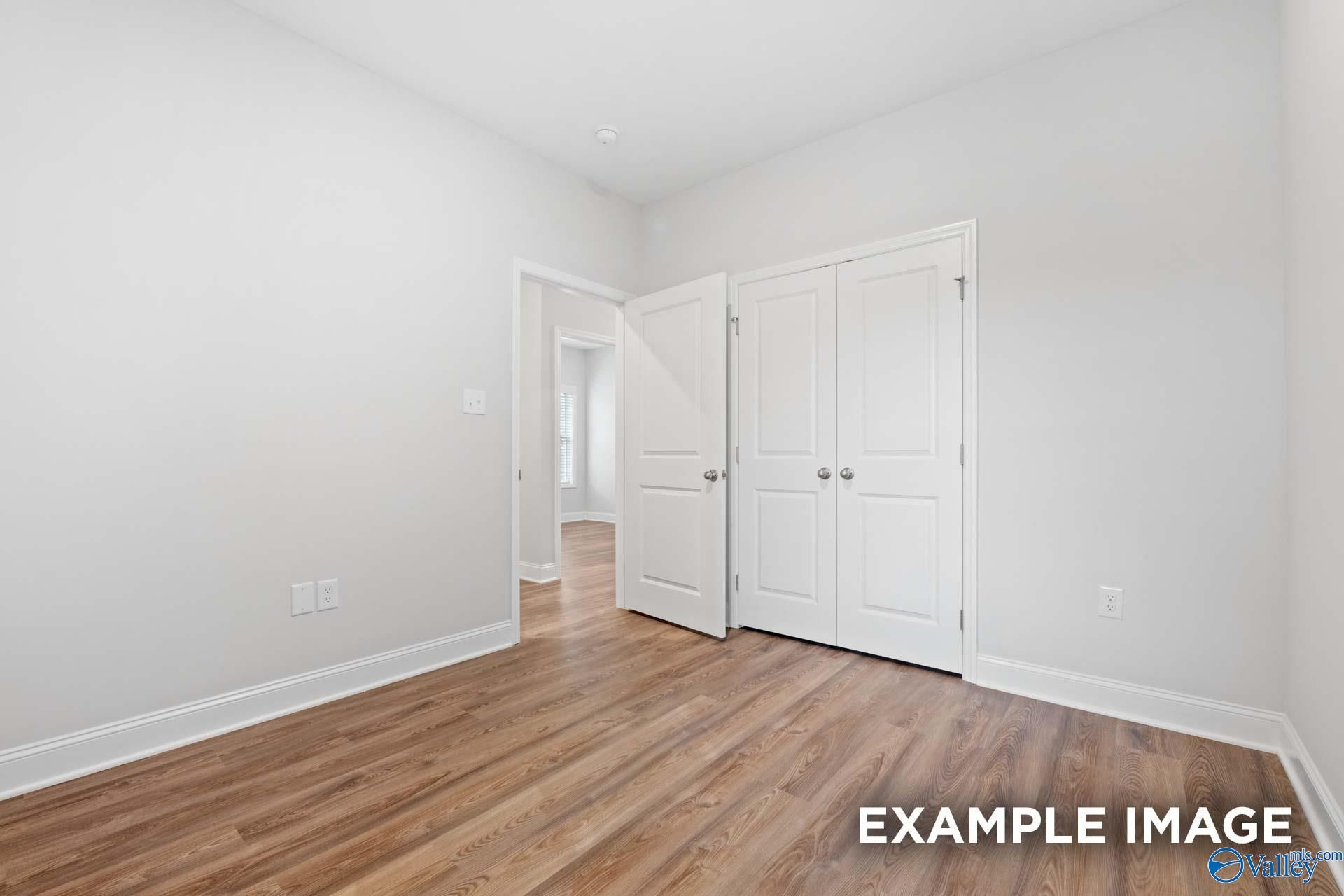 Bright bedroom featuring open double doors to walk-in closet, white walls, luxury vinyl plank floors in Davidson Homes The Cumberland, Decatur AL
