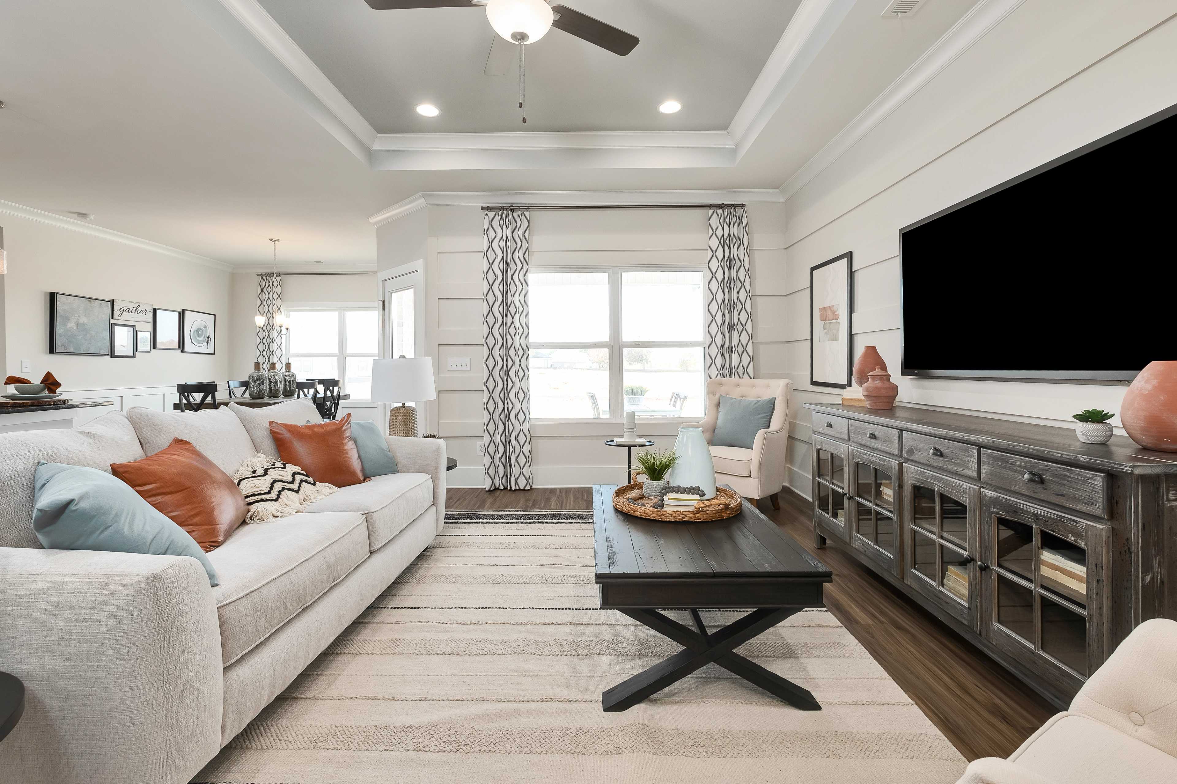 Open-concept living room at Mallard Landing in Athens Alabama with neutral sectional sofa, wooden coffee table, and large curtained windows
