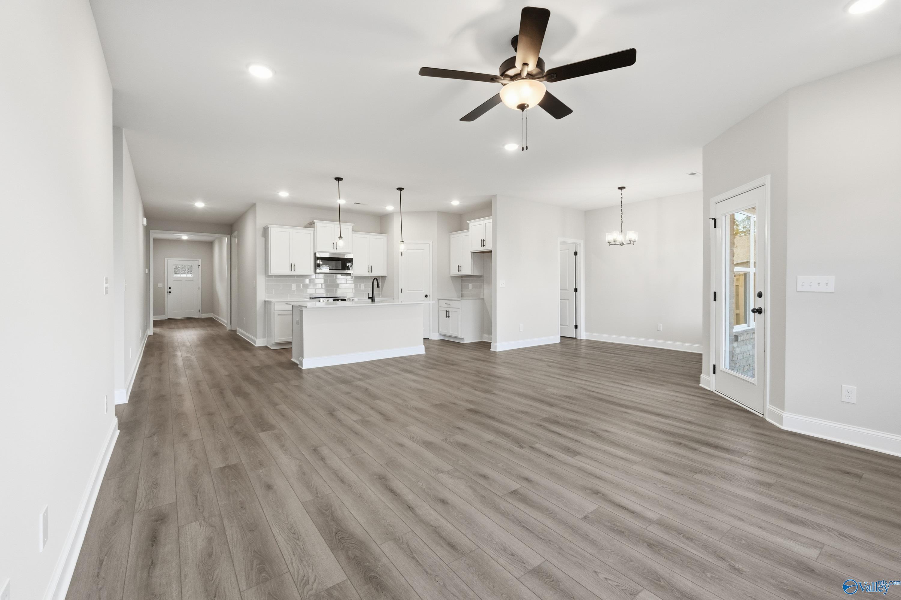 Open-concept living and kitchen space with white cabinets, large island, ceiling fan, and luxury vinyl plank flooring in The Daphne D by Davidson Homes, Arab, Alabama