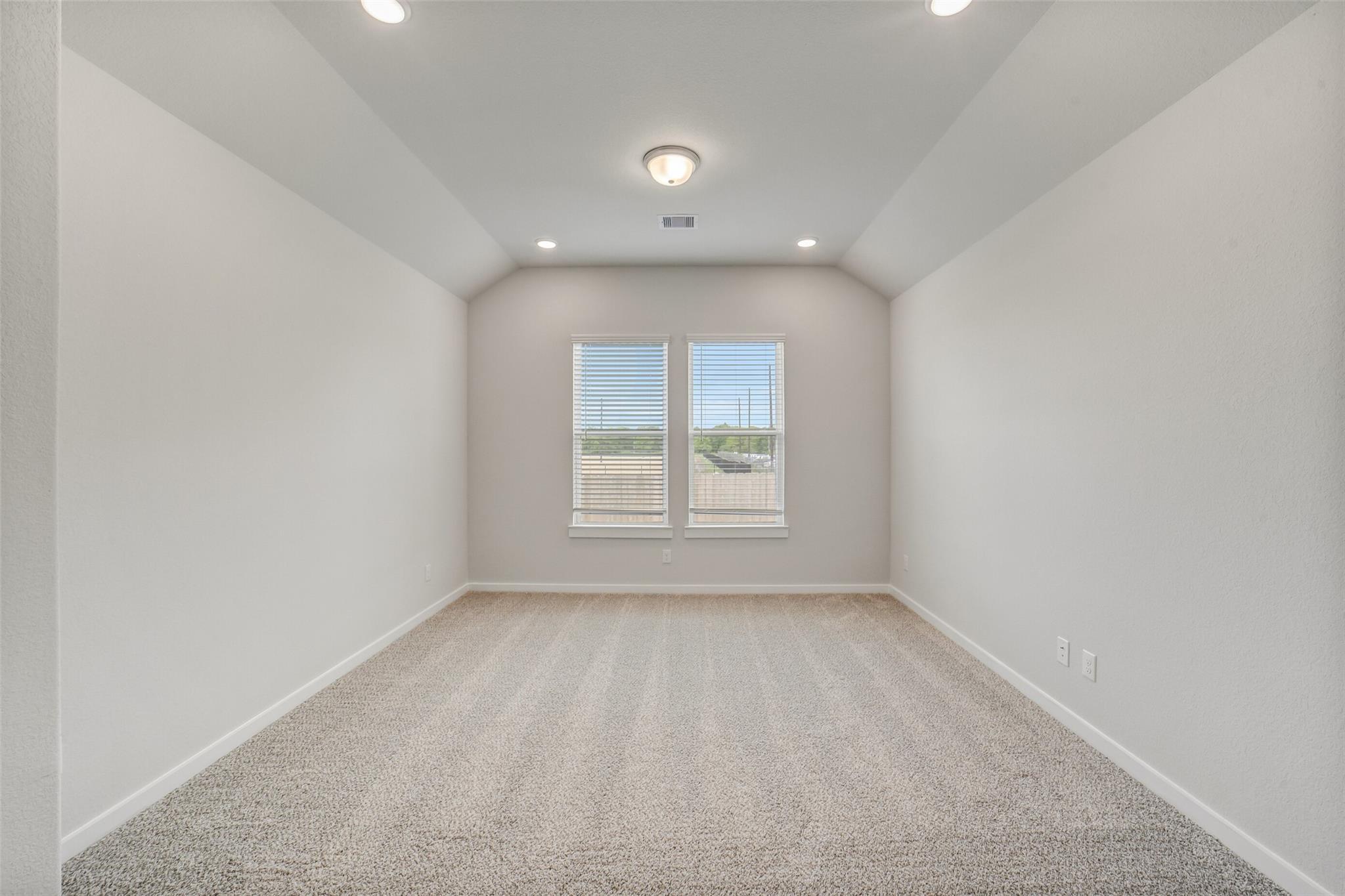 Bright empty bedroom with beige carpet, neutral walls, large shuttered windows, vaulted ceiling and recessed lights in The Acadia C, Magnolia TX