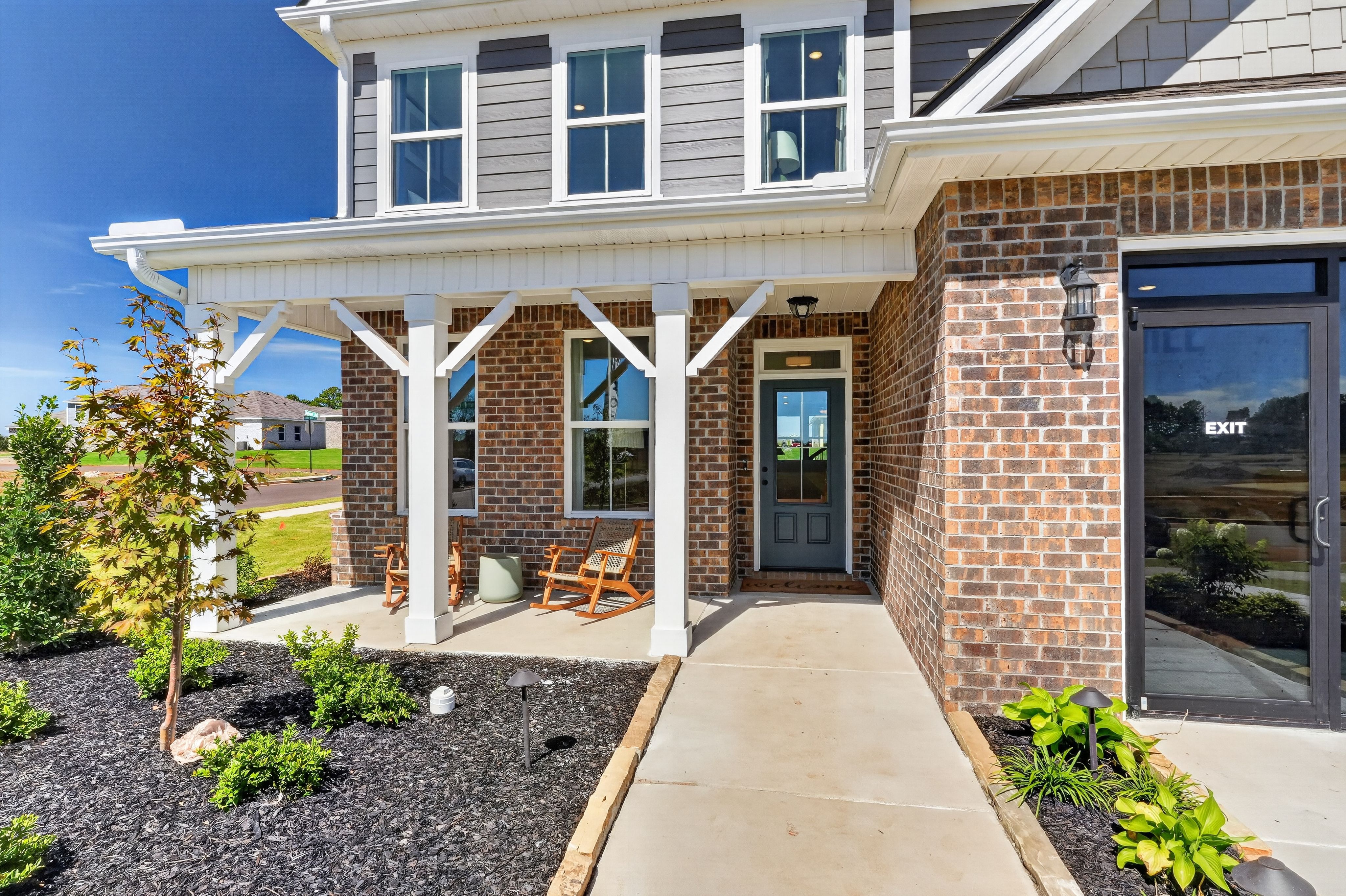 Brick and gray two-story home with covered front porch and rocking chairs at Evergreen Mill by Davidson Homes in Madison, Alabama