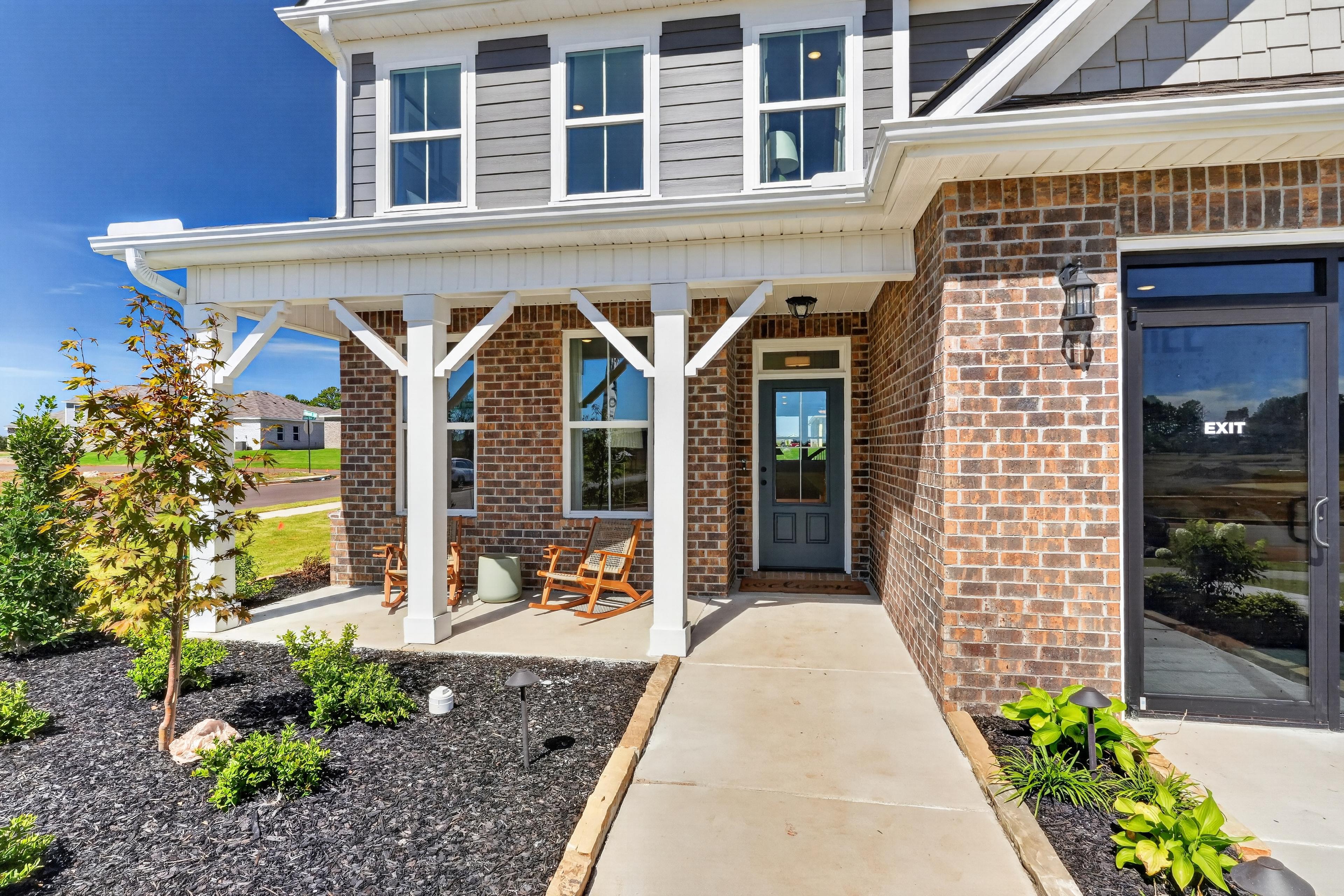 Brick and gray two-story home with covered front porch and rocking chairs at Evergreen Mill by Davidson Homes in Madison, Alabama