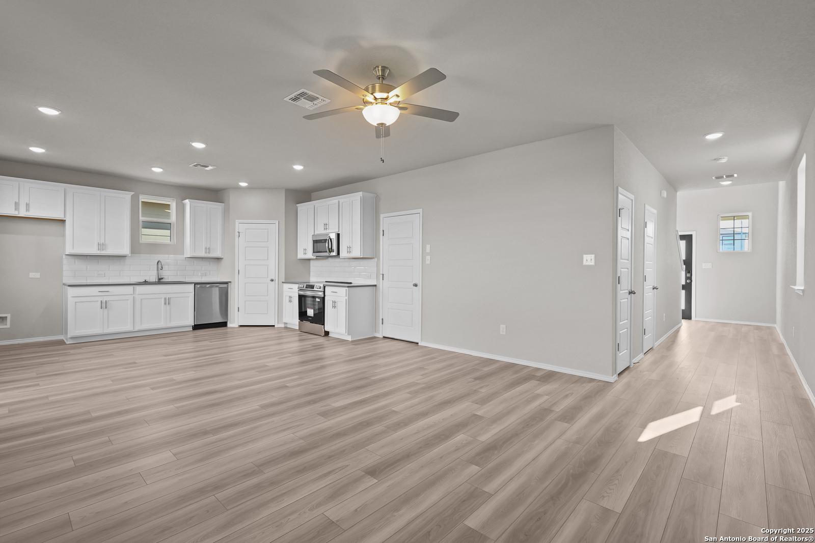 Open-concept kitchen with white cabinets, stainless appliances, and luxury vinyl plank floors in Davidson Homes Trinity D, San Antonio